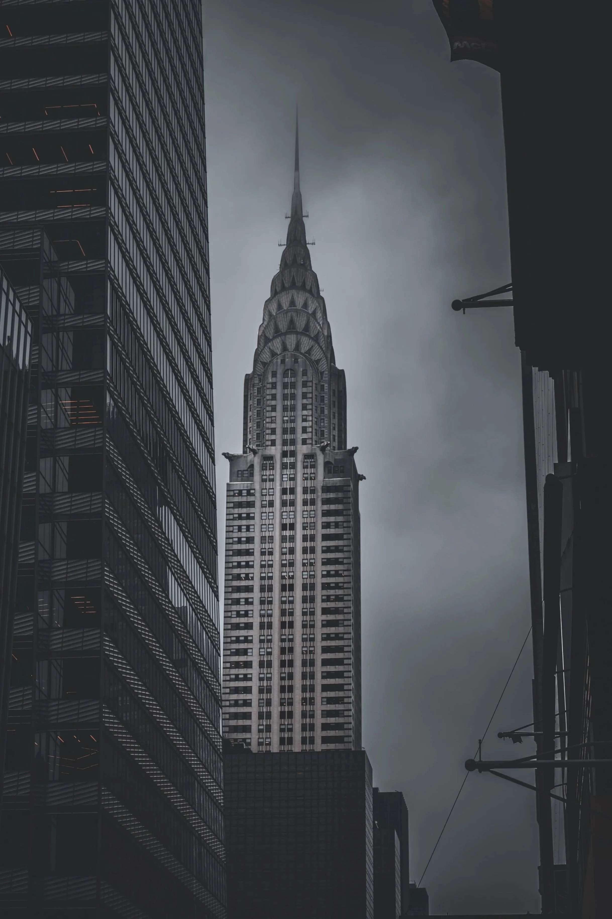 The image shows a view of the Chrysler Building, an iconic Art Deco skyscraper in New York City, surrounded by other tall buildings under a cloudy sky.