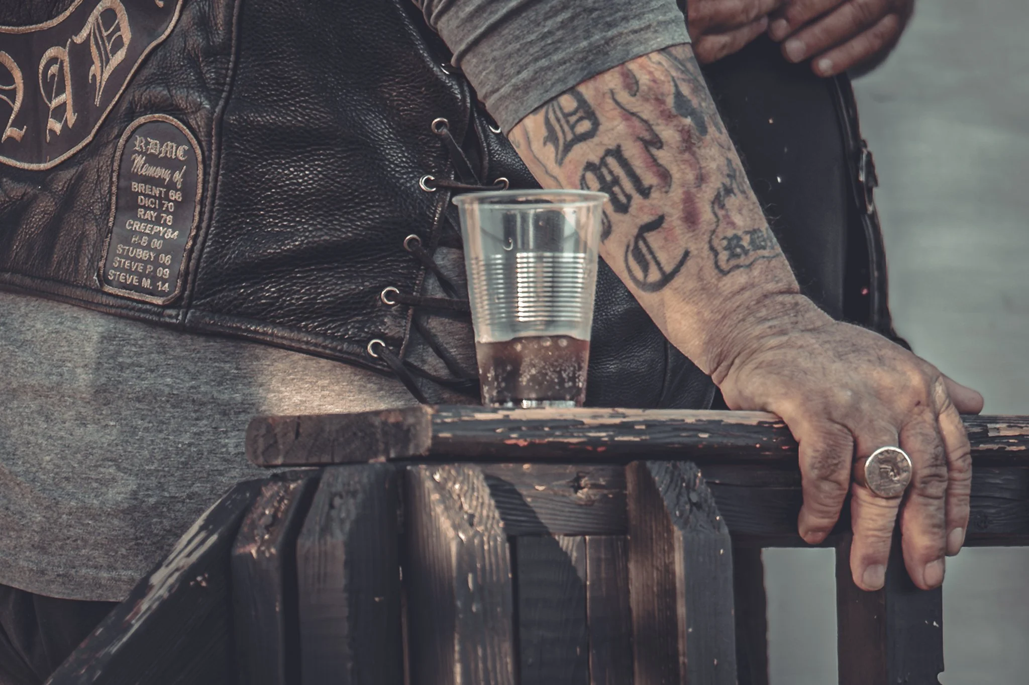 Close-up of a person's arm with tattoos resting on a wooden railing, with a drink placed on the railing.