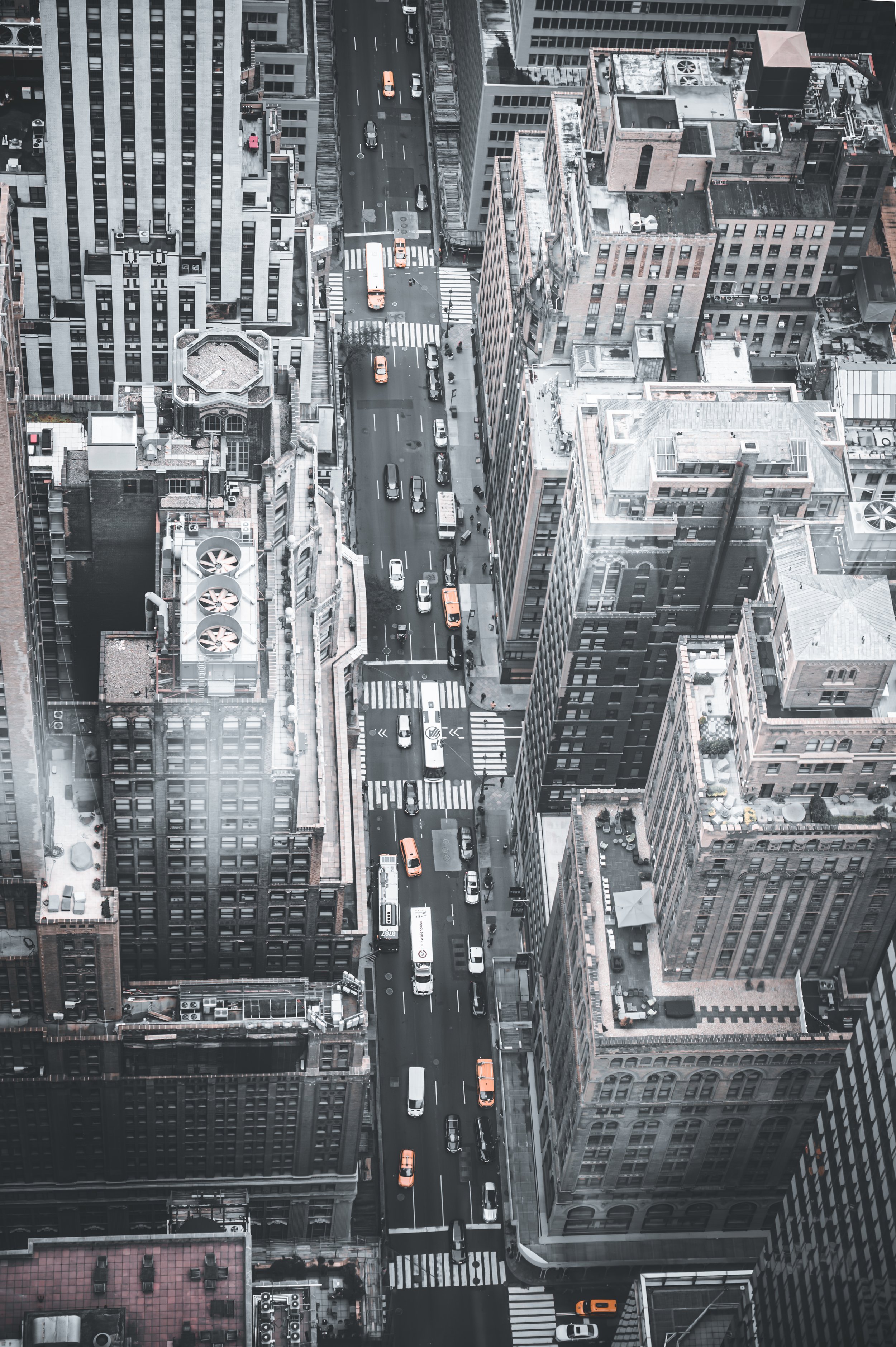 Bird's eye view of a city street surrounded by tall buildings, with cars and buses on the road and crosswalks at intersections.