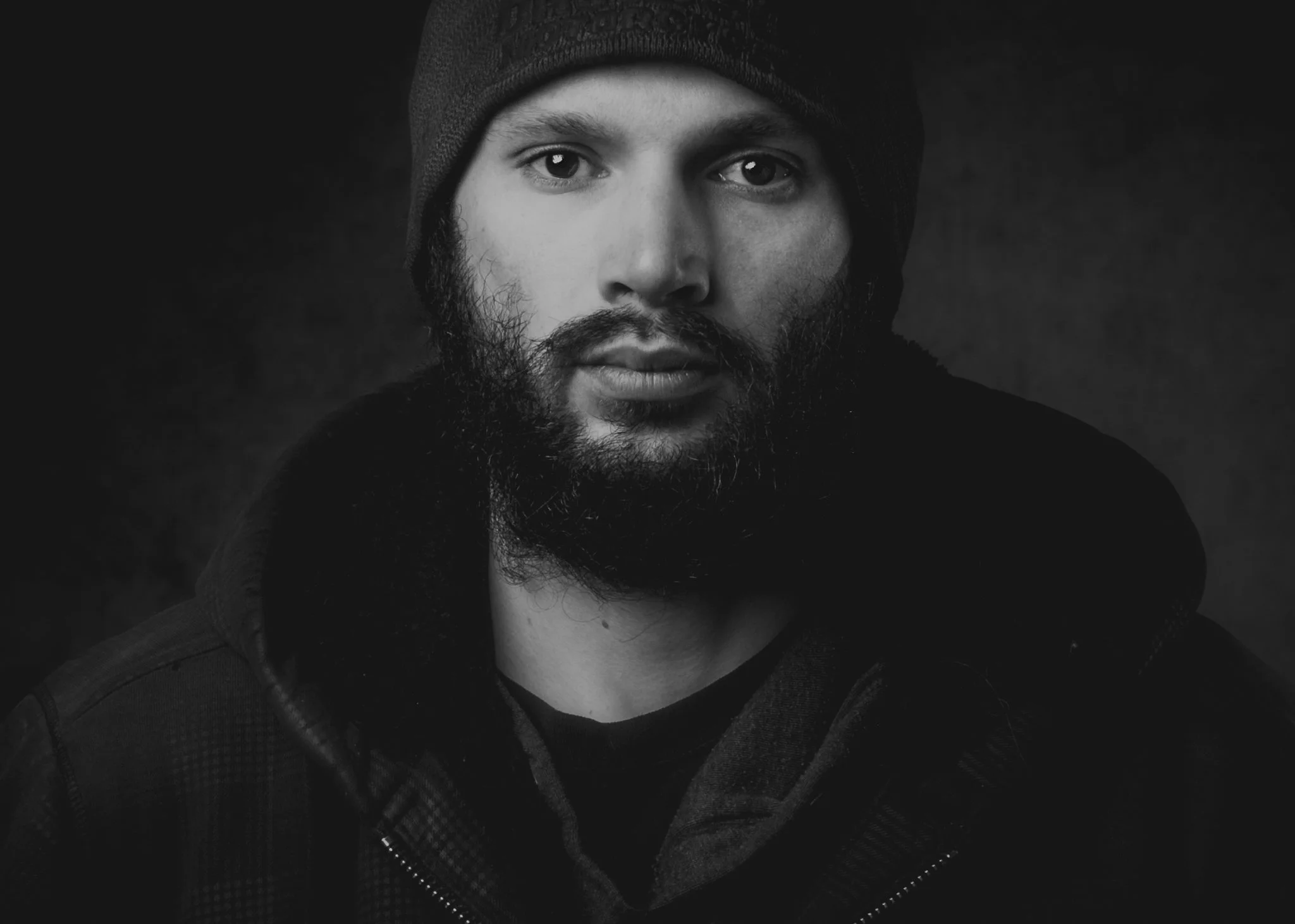 Black and white portrait of a man with a beard wearing a toque and a jacket, looking directly at the camera.