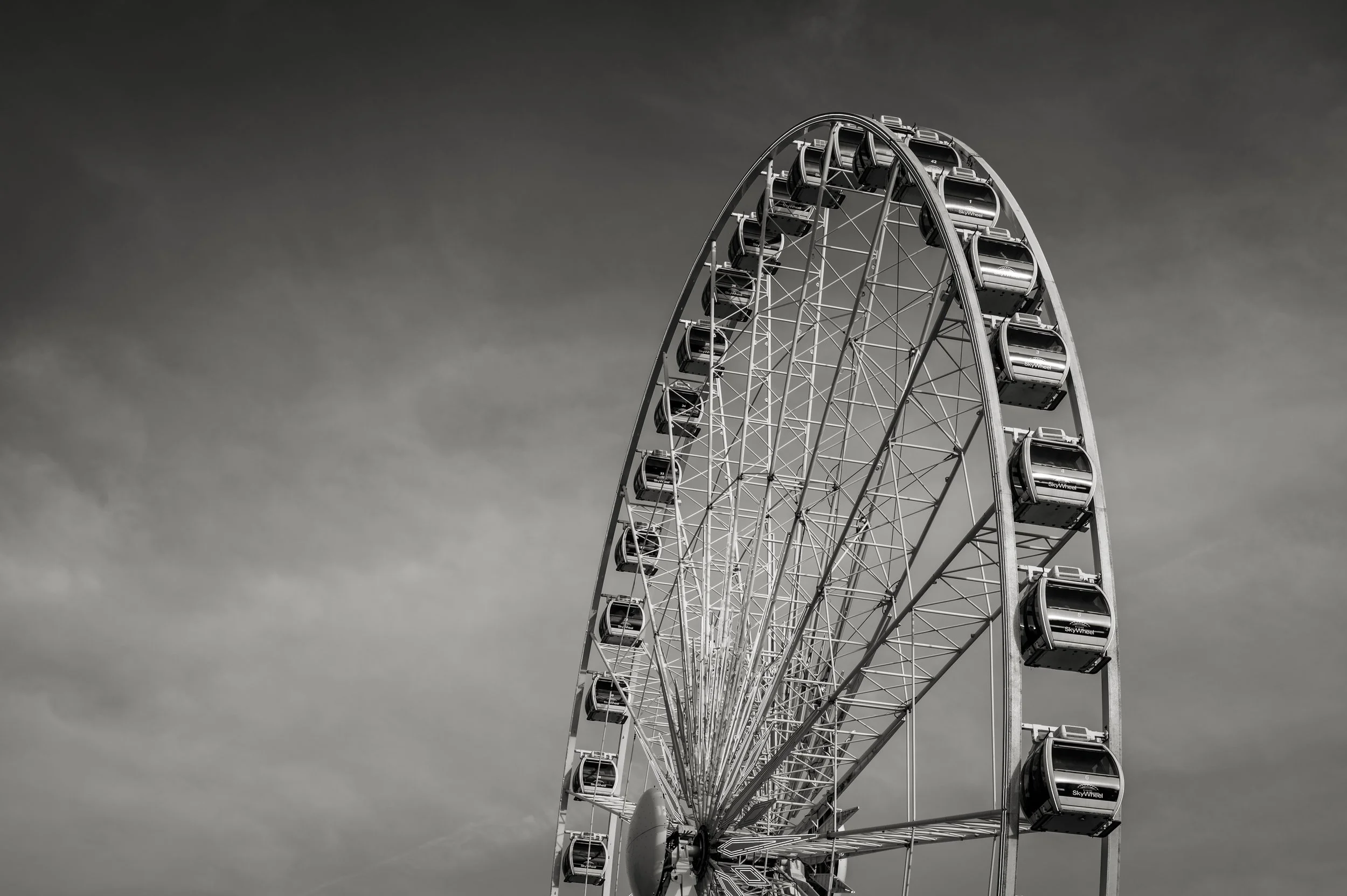 Black and white photo of a large Ferris wheel against a cloudy sky.