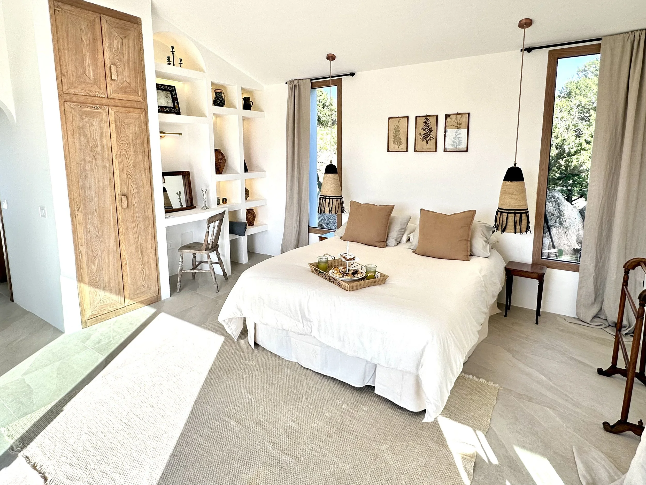 A minimalist bedroom wabi-sabi style with a white bed, two narrow windows, and a wall art with the letter U in black, all in a neutral color palette with natural wood accents.