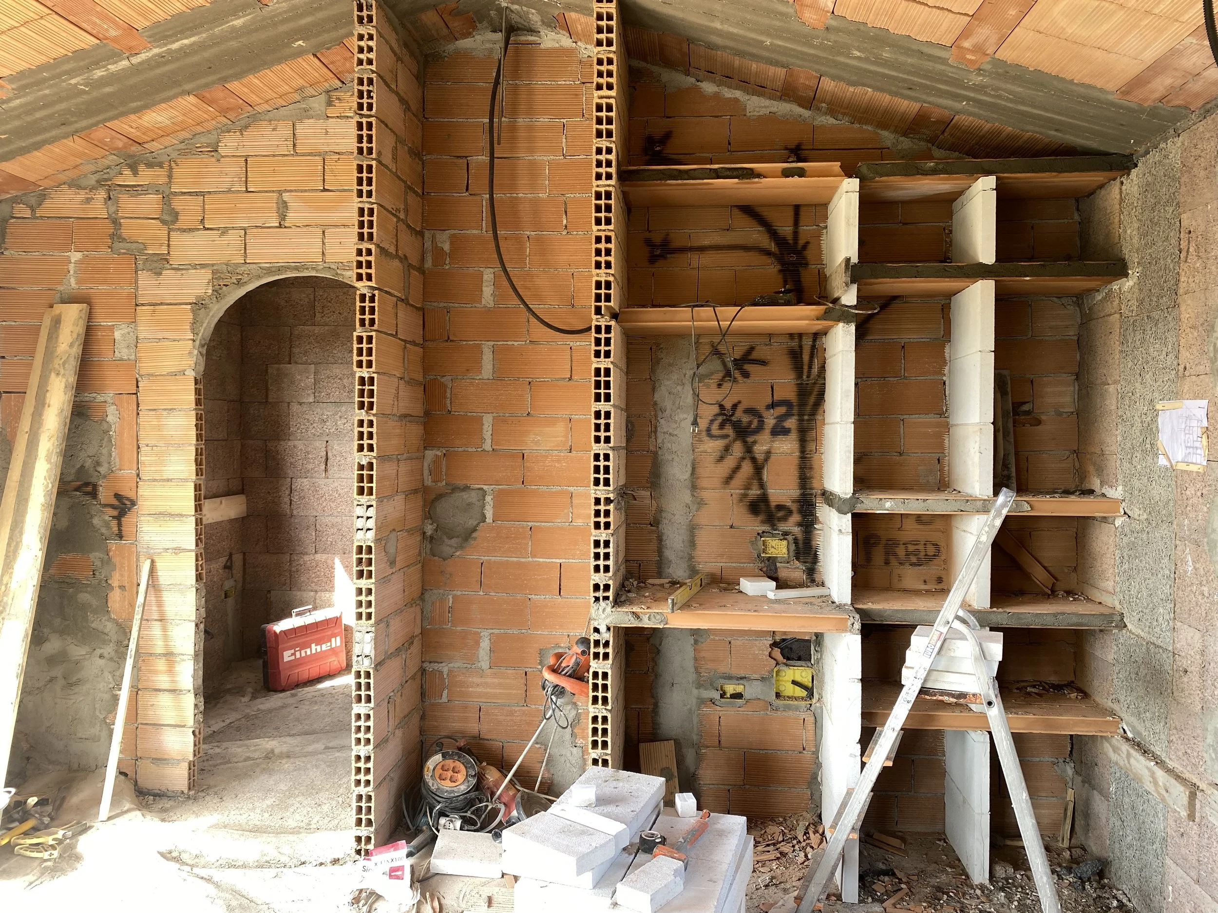 Construction site showing brick walls, wooden shelves, and construction tools, with electrical wiring visible.