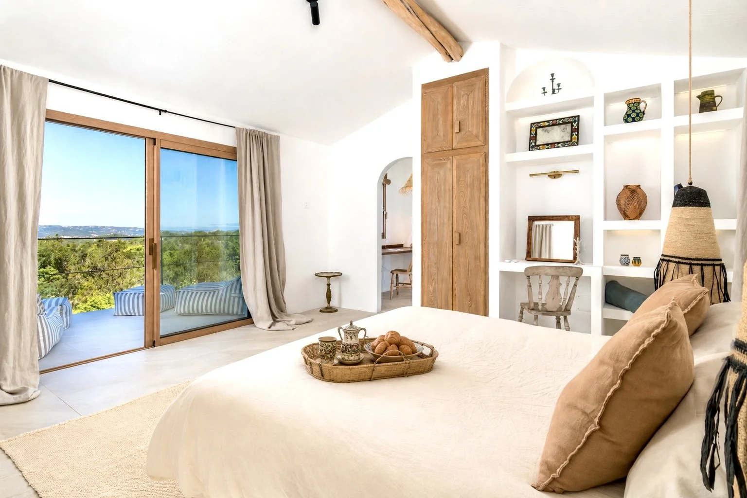 A minimalist bedroom wabi-sabi style with a white bed, two narrow windows, and a wall art with the letter U in black, all in a neutral color palette with natural wood accents.
