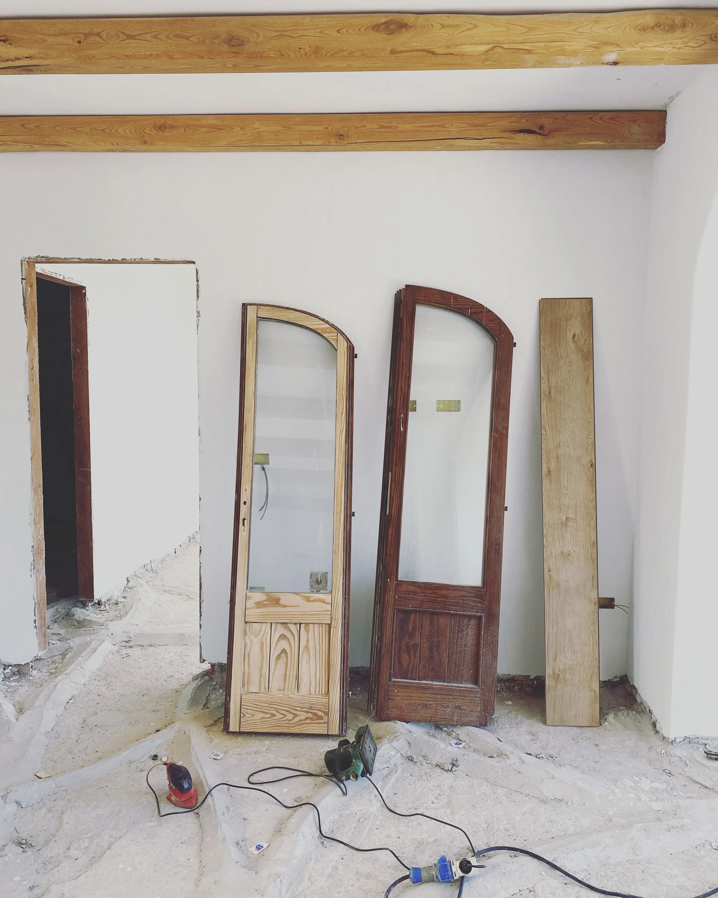Interior room under construction with three wooden doors and construction tools on the floor.