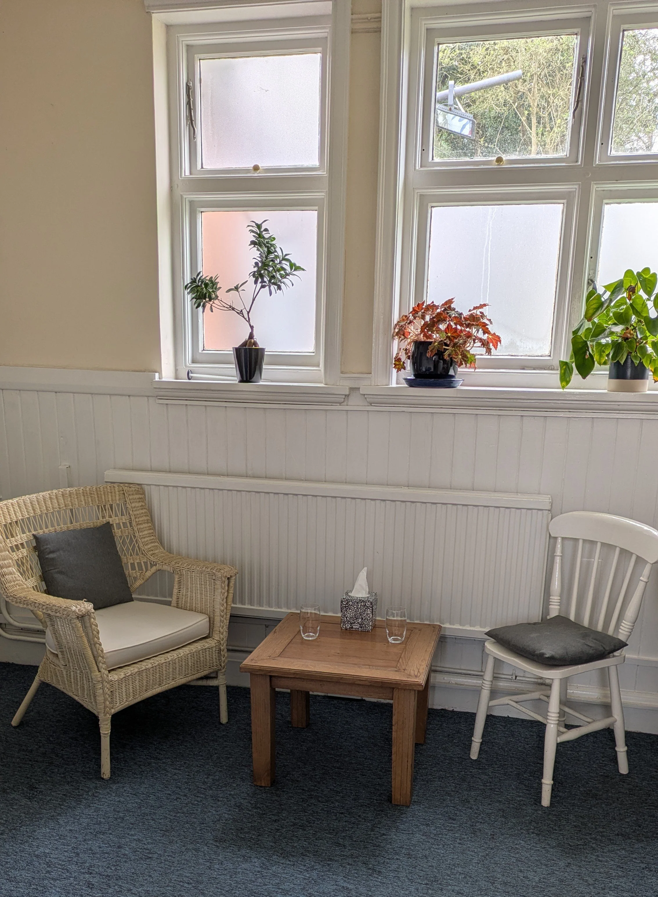 Bright Witney therapy room with wicker and wooden chairs, plants, and natural light at The Authentic Space Therapy.