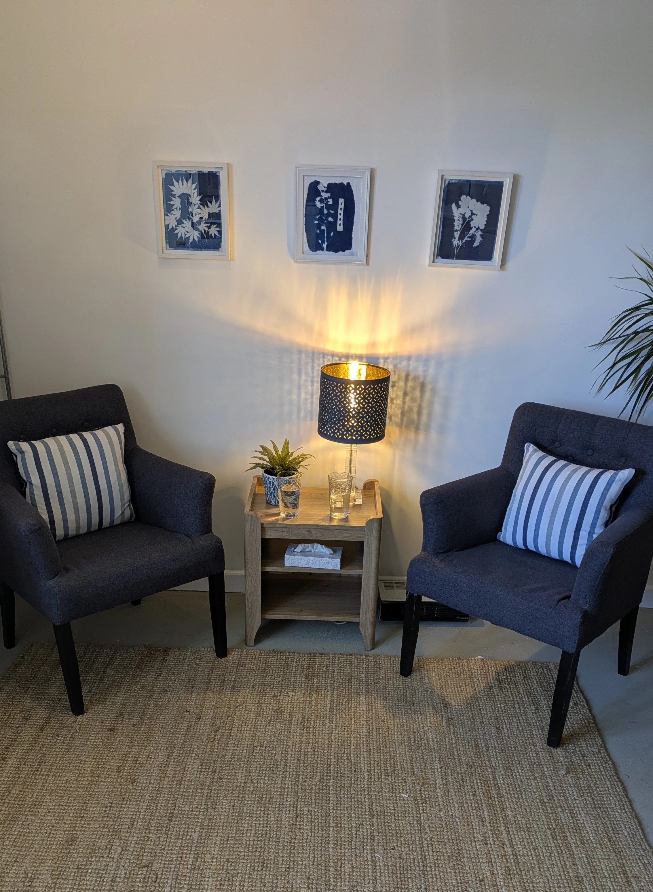 Cozy therapy room in Witney with navy armchairs, striped cushions, a warm lamp, and jute rug at The Authentic Space