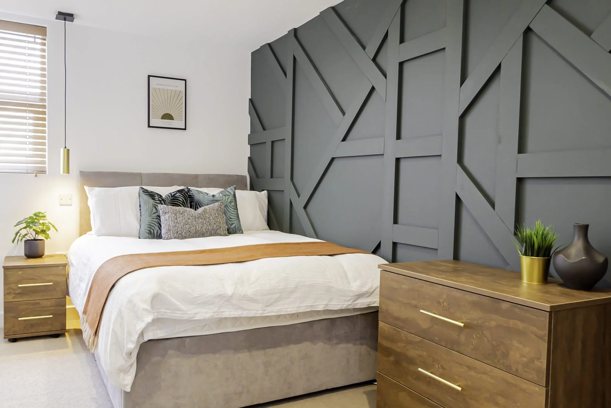 Modern bedroom with a white bed, patterned pillows, wooden nightstands, and a feature wall with geometric gray panels.