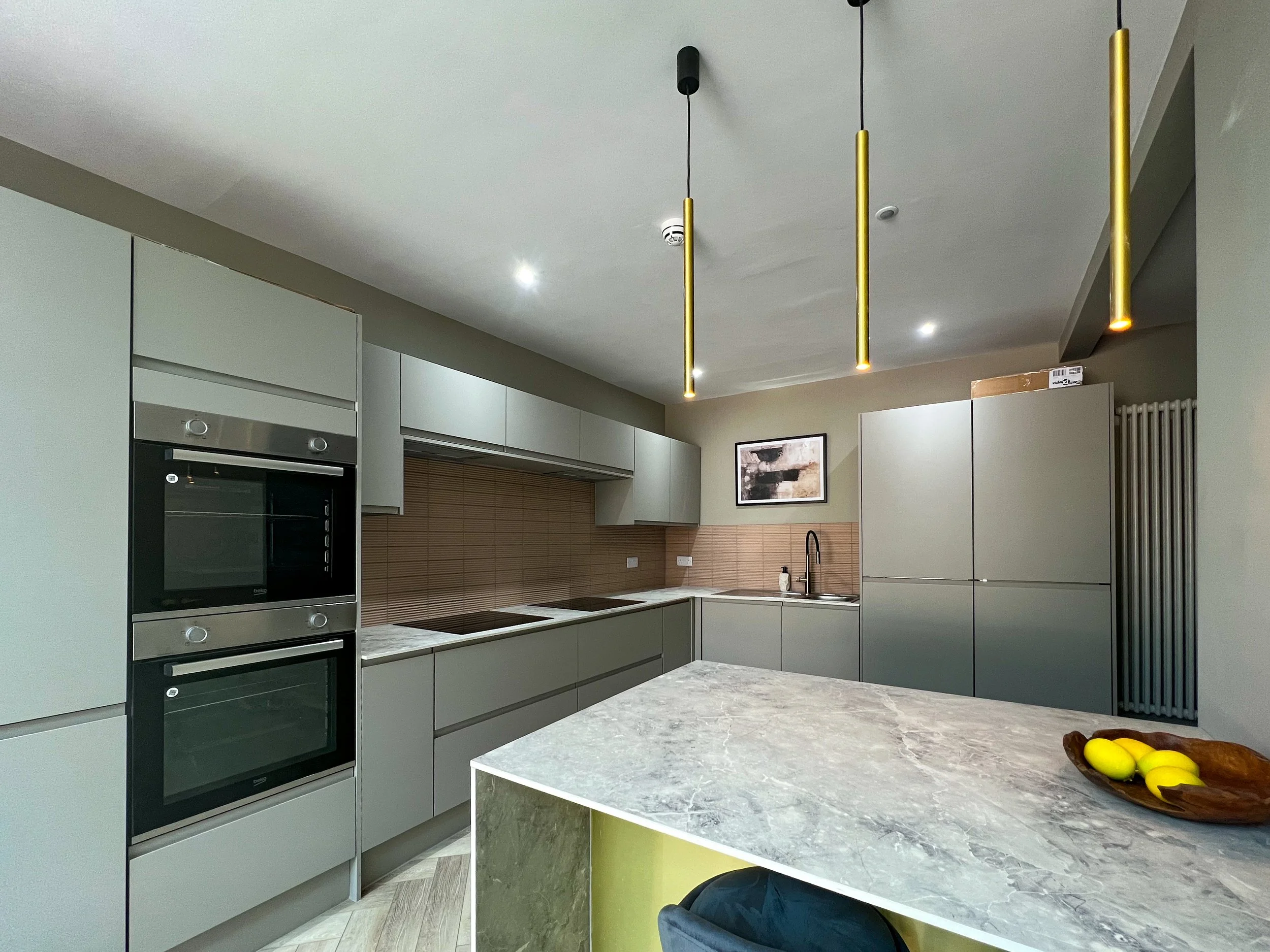 Modern kitchen with gray cabinets, a marble island, pendant lights, and a small framed artwork on the wall.