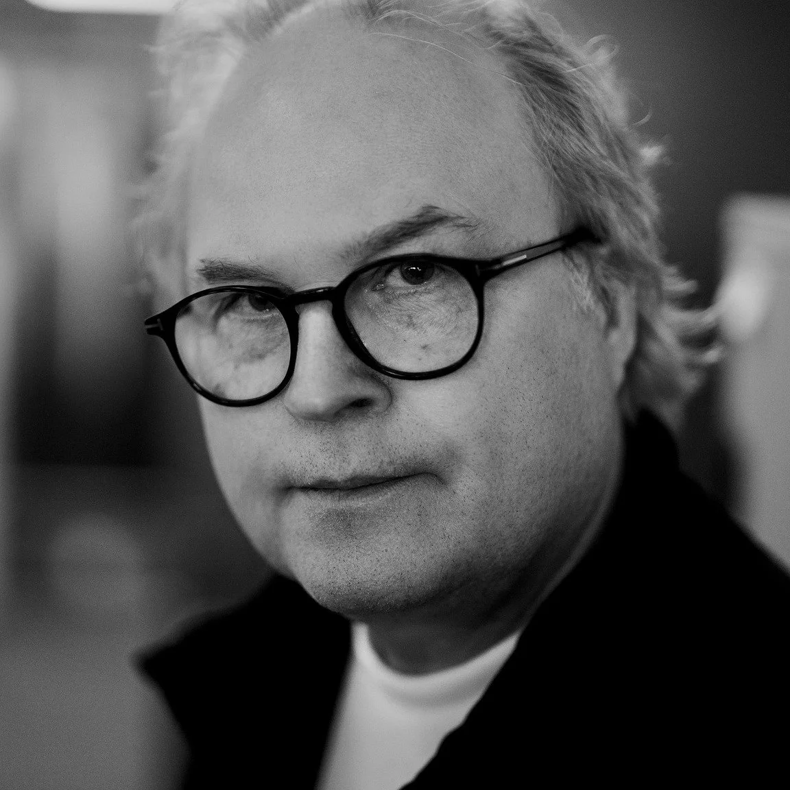 Black and white close-up portrait of a man with glasses and wavy gray hair.