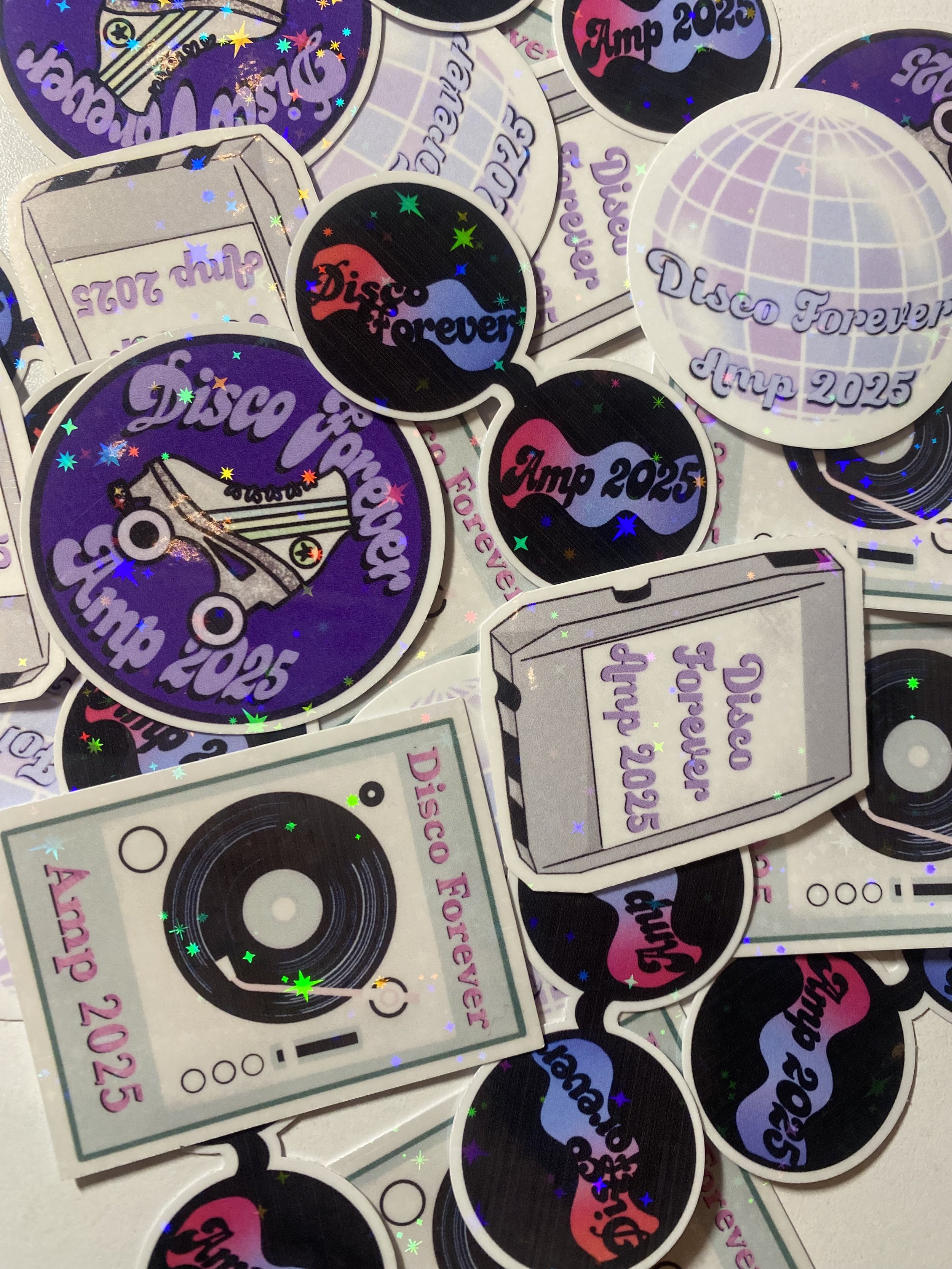 Collection of holographic stickers with retro and disco-themed designs, including a disco ball, a cassette tape, a pair of sunglasses, and the phrases 'Disco Forever', 'Amp 2025'