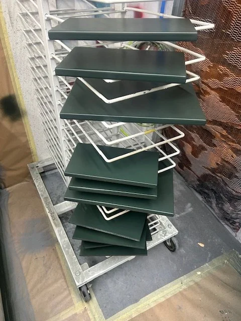 A display rack with multiple green rectangular trays, some tilted, with white wire support frames, placed on a metal cart in a retail or storage area.