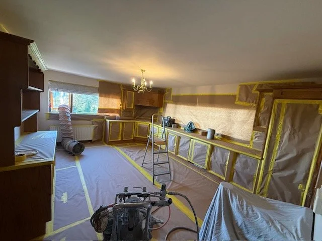 Room under renovation with cabinets covered in brown paper and yellow painters tape, ladder, and renovation tools.