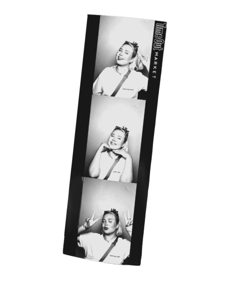 A photo booth strip with three black-and-white pictures of a young woman making different playful expressions and gestures, including smiling, resting her chin on her hands, and making peace signs.