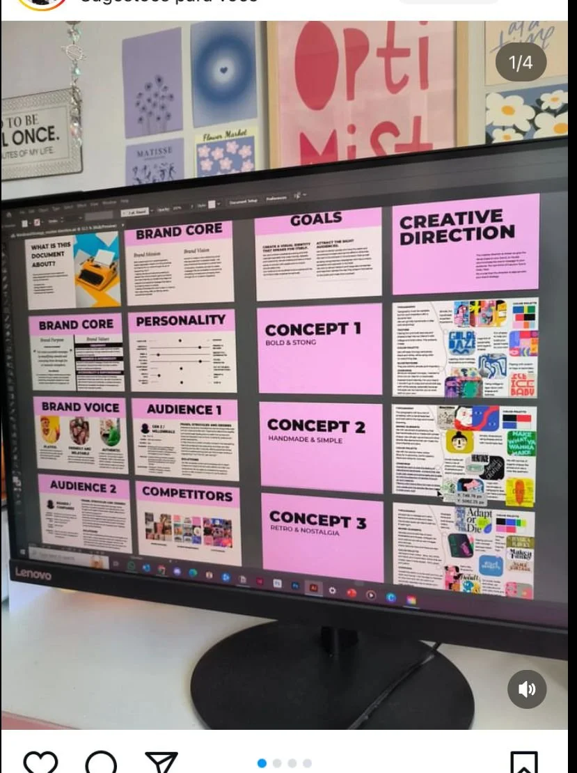 A computer monitor displaying a presentation slide with branding and creative direction sections, including goals, personality, audience, competitors, and concepts, in a pink and white color scheme. In the background, there are posters and artwork on the wall.