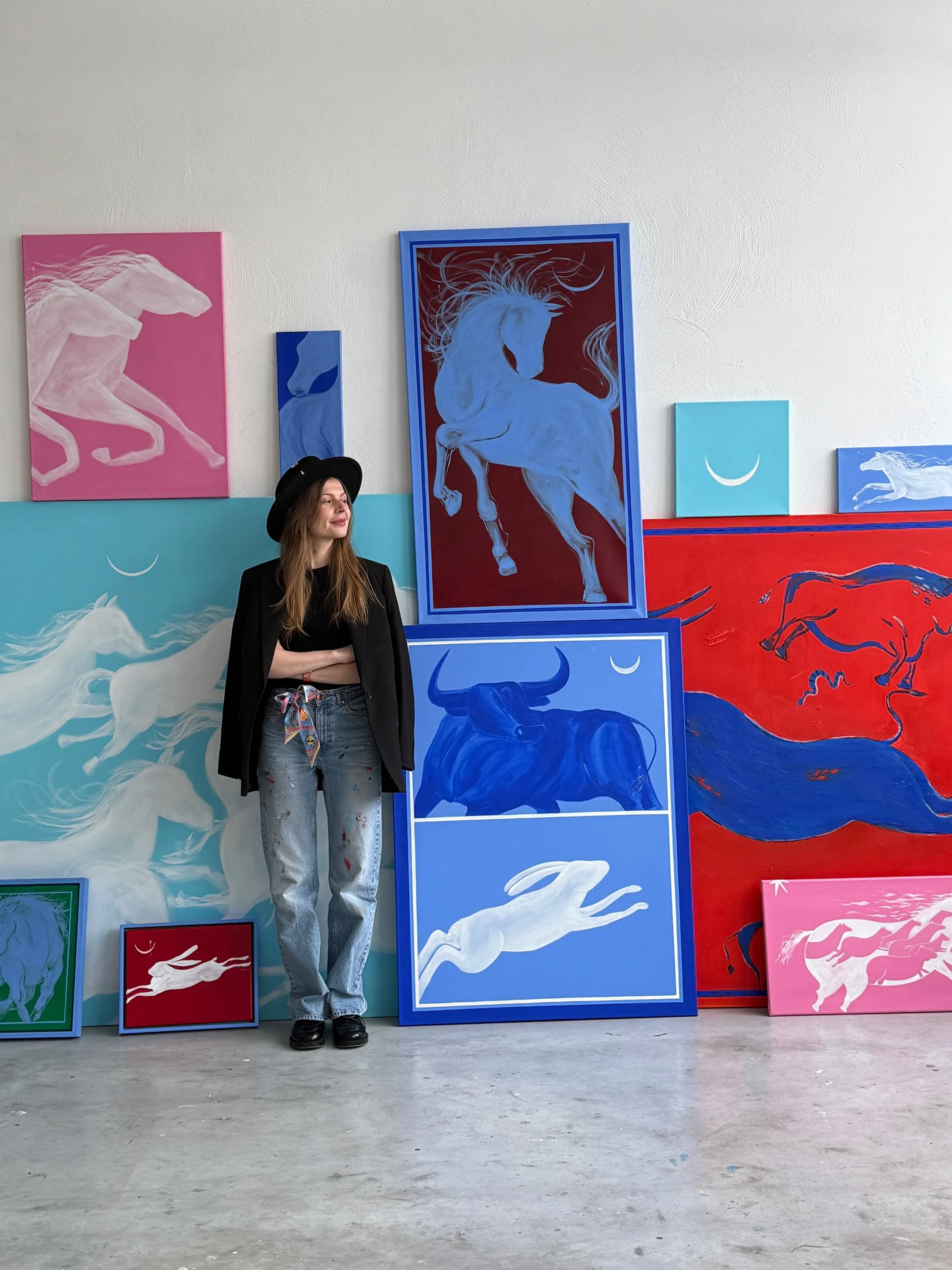 Contemporary artist Jevgenia Vassiljeva standing in her studio surrounded by large colorful animal paintings from the Loovart collection