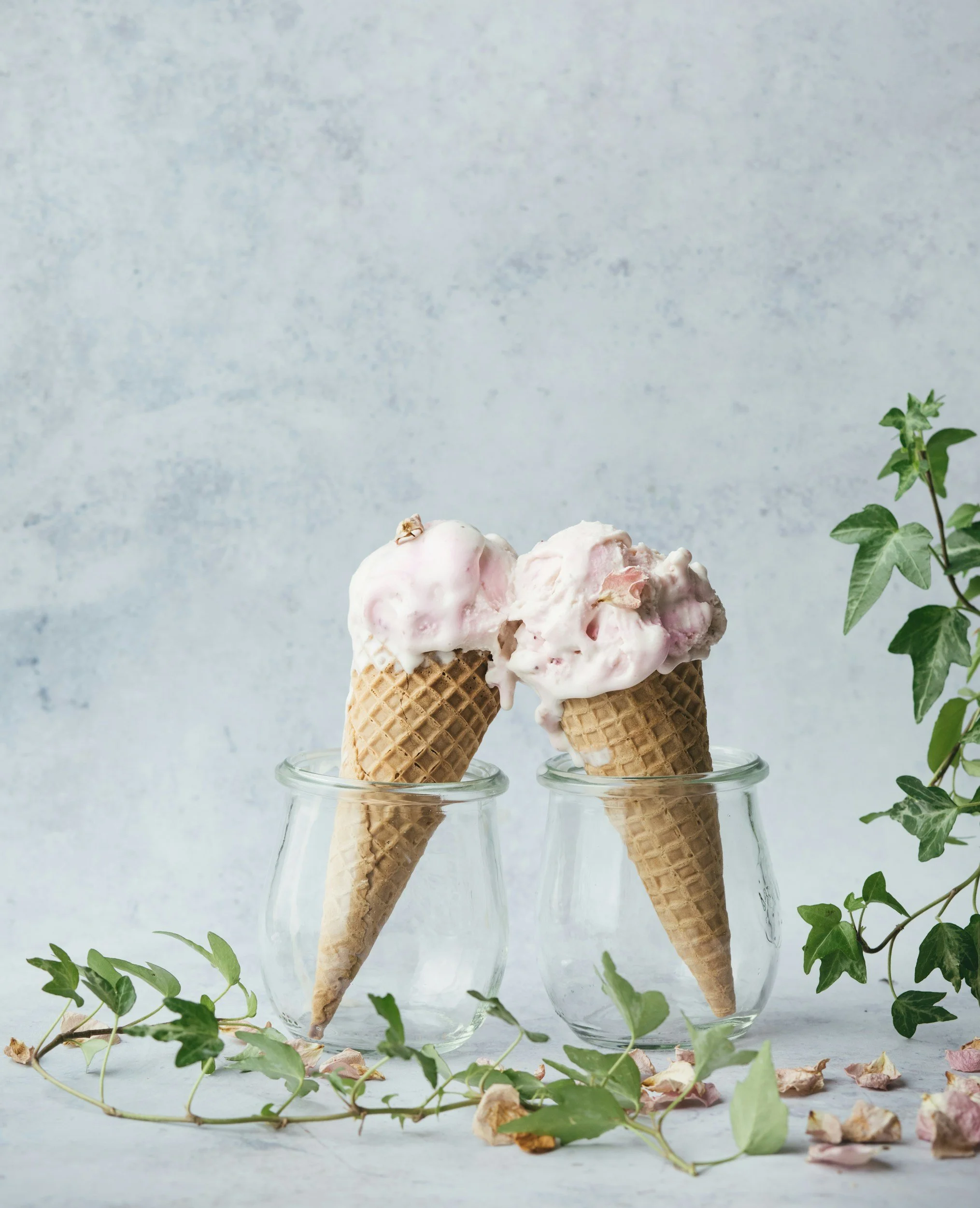 Two ice cream cones held by glasses pictured against a grey background