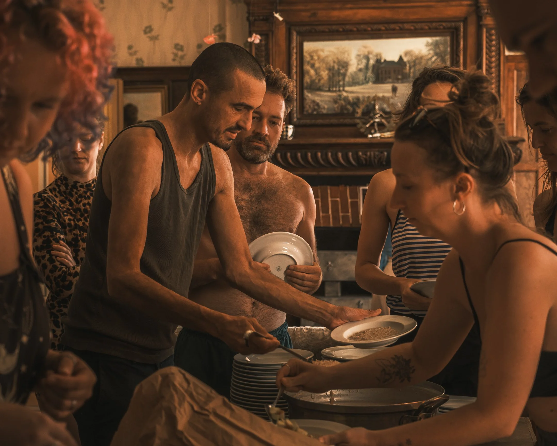 Mensen staan in een rij in een keuken, ze eten uit borden, in een warme en gezellige kamer met houtdecor.