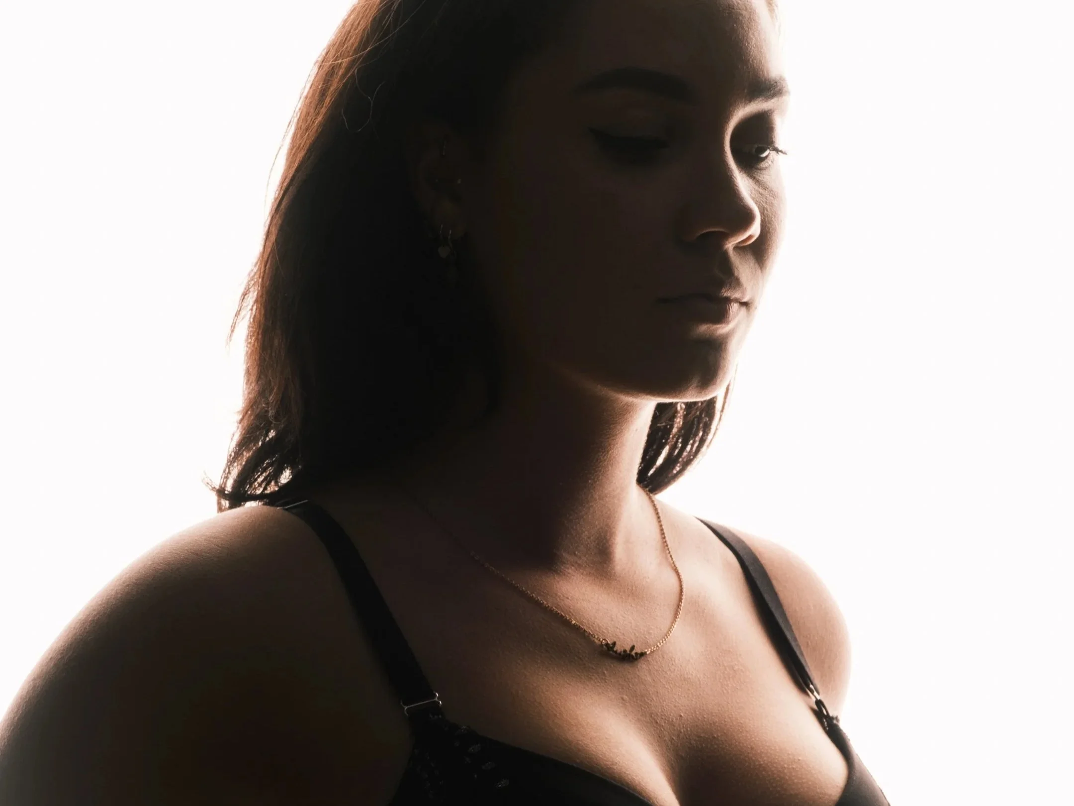 Portret van een vrouw met gesloten ogen, donkere achtergrond en zacht licht op haar gezicht en schouders.