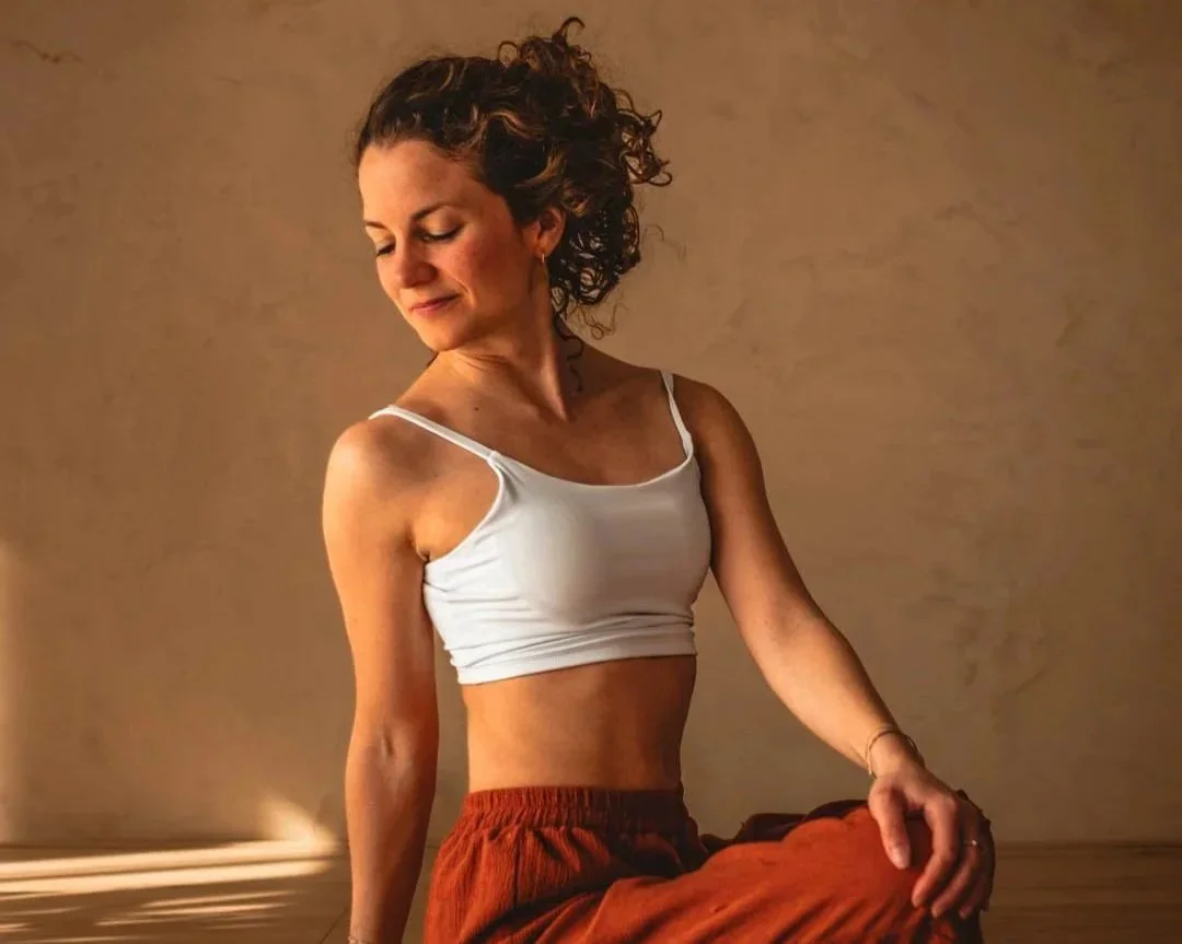 Vrouw die in lotushouding mediteert, zit op de vloer in een kamer met een effen muur achter haar.