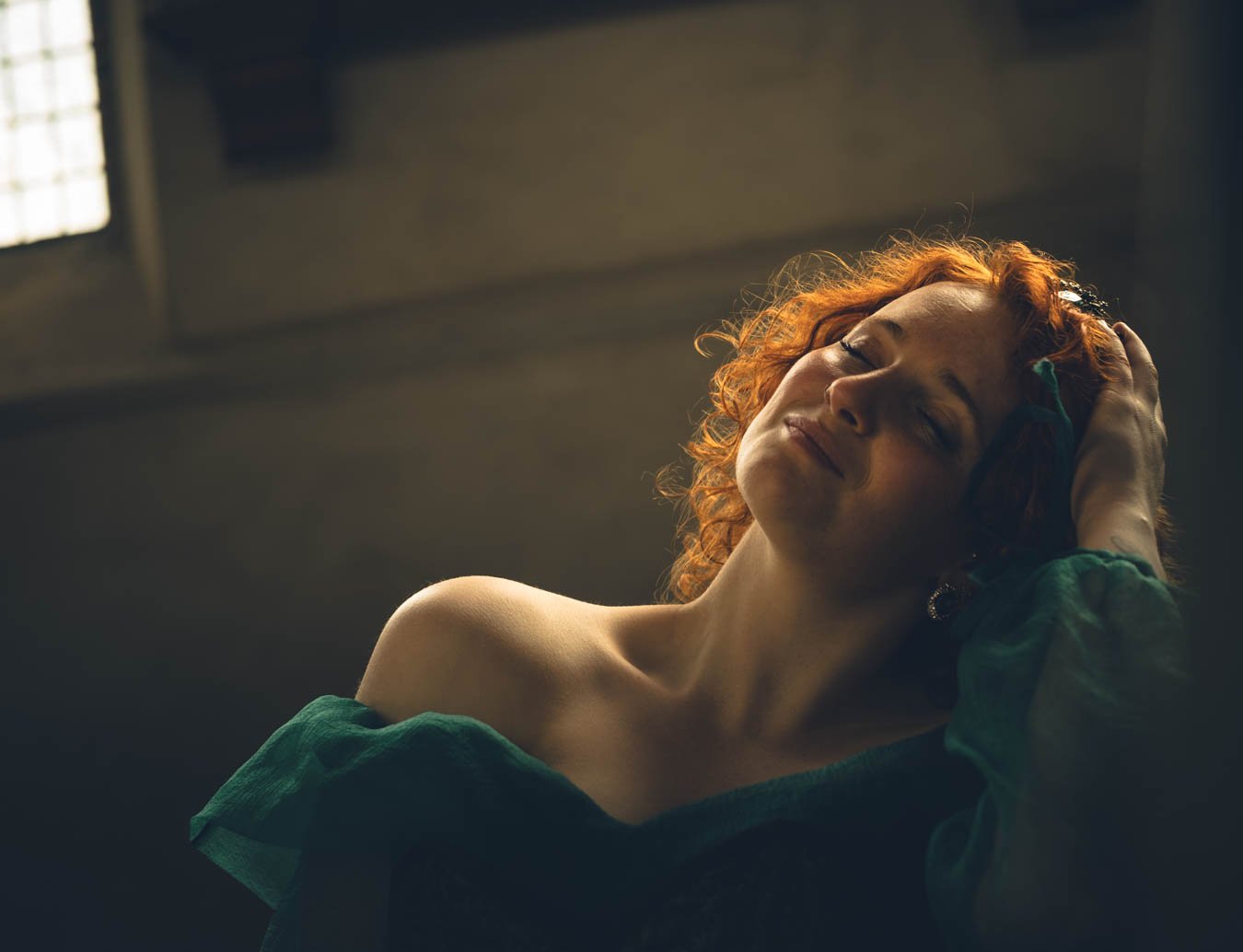 Vrouw met rode haar ligt met gesloten ogen, haar hand op haar hoofd, in een kamer met licht van een raam.