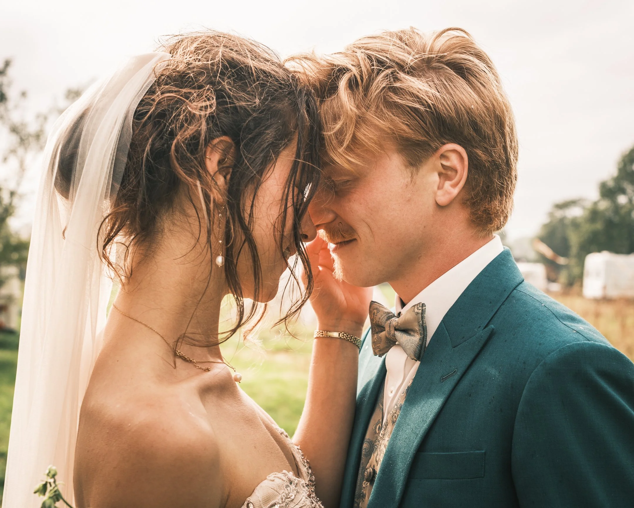 Een bruid en bruidegom die elkaar met voorhoofd tegen voorhoofd aanraken tijdens hun huwelijk buiten.