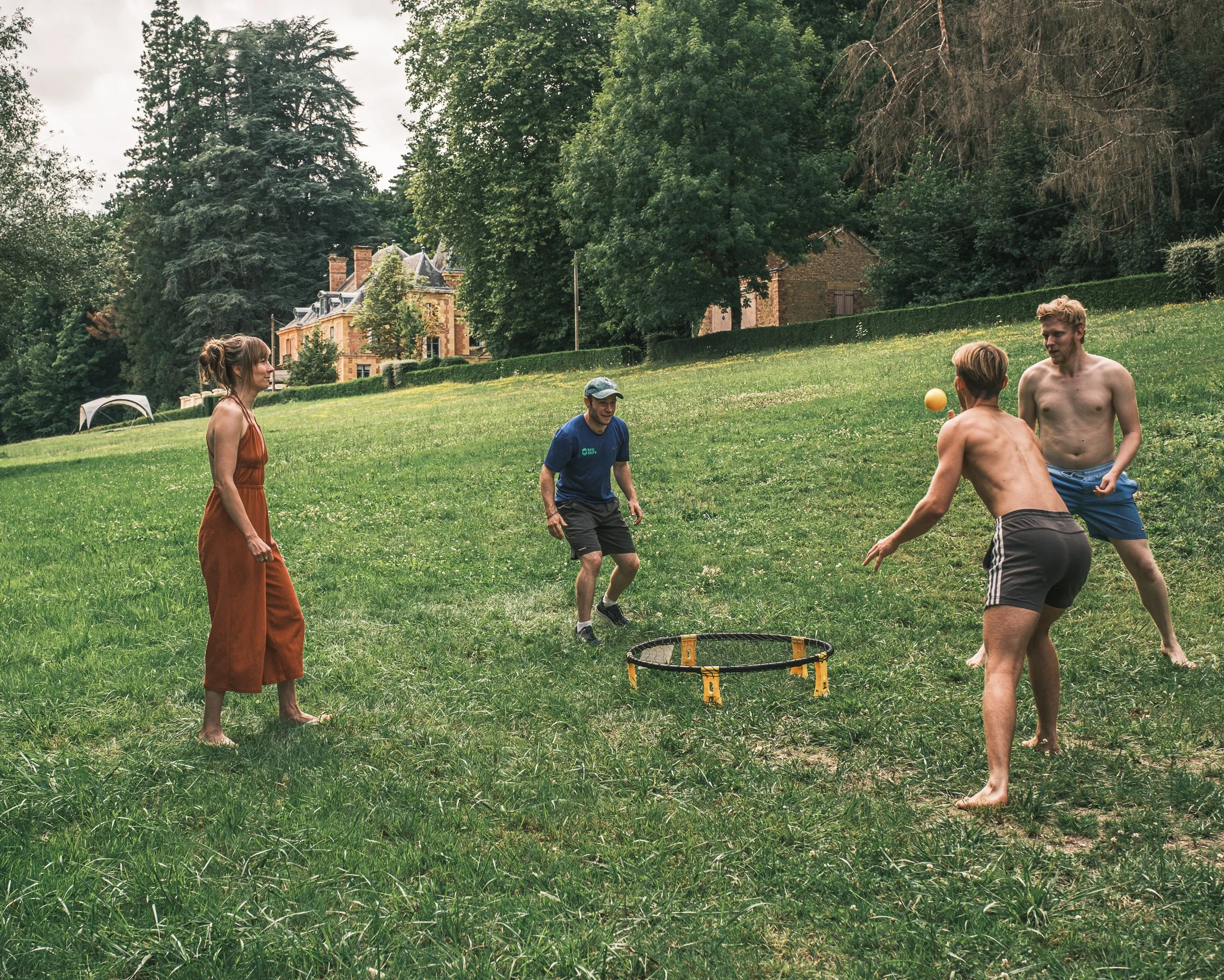 Vijf mensen die een game in een open grasveld spelen, met bomen en huizen op de achtergrond.