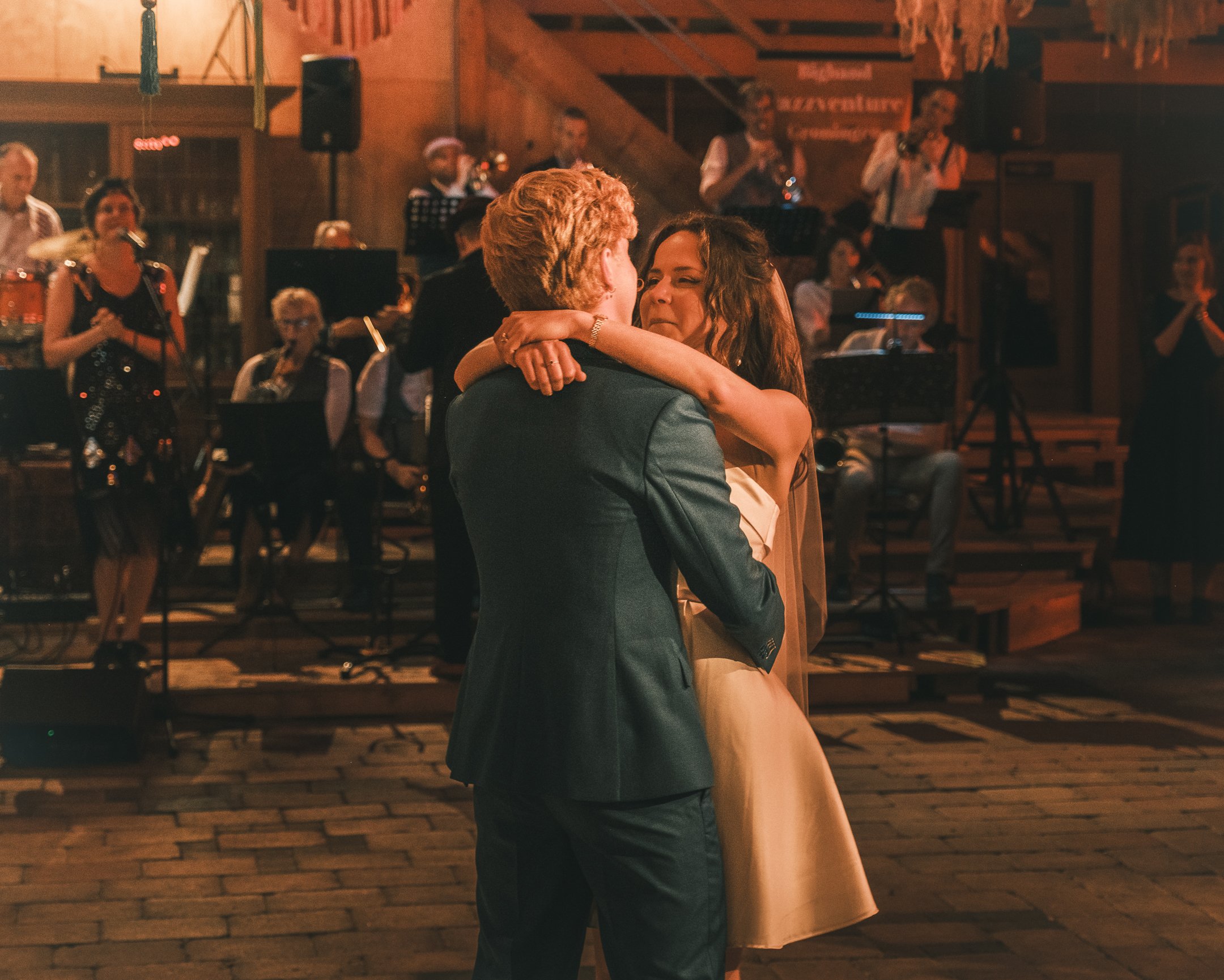 A couple is dancing closely together at a wedding reception, with a band playing live music in the background.