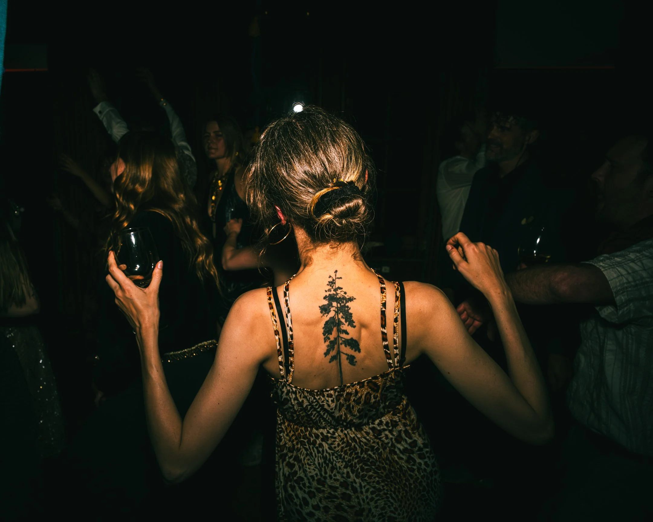 Een vrouw met een grote tatoeage van een dennenboom op haar rug in een donkere, feestelijke omgeving.