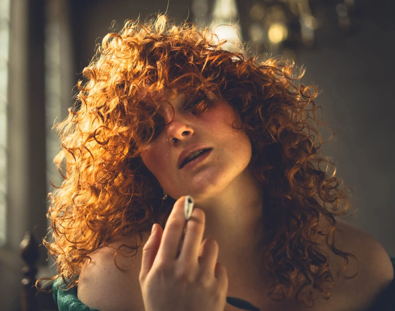 Portret van een vrouw met krullend rood haar, die een sigaret vasthoudt, in een binnenruimte met natuurlijk licht.