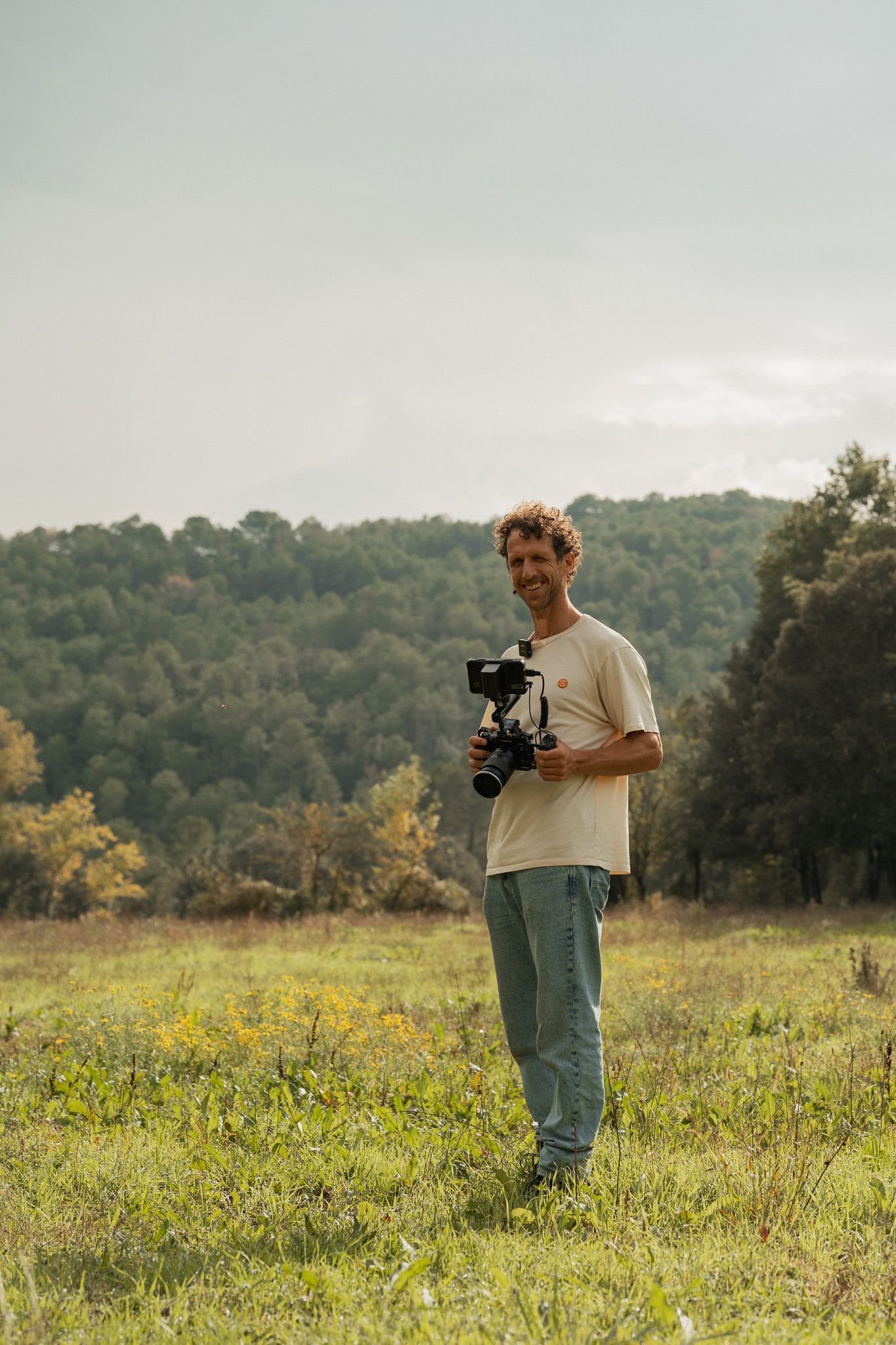 Man met camera in een veld met bomen op de achtergrond.