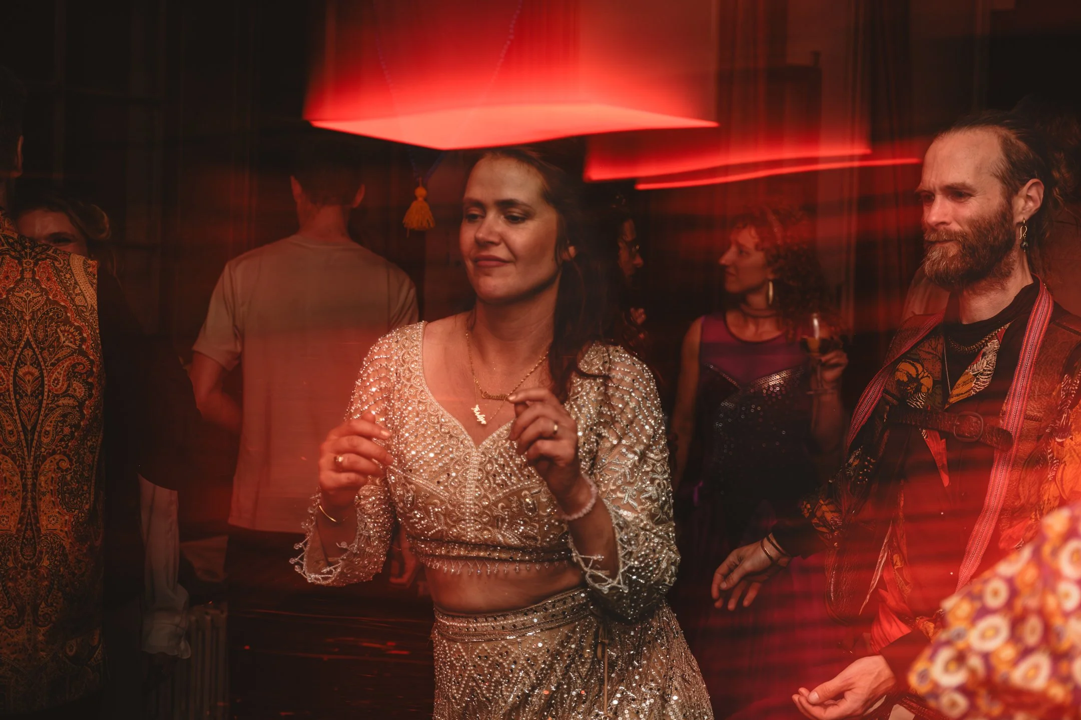 Mensen dansen bij een feestje, met rode verlichting en een gedrapeerde achtergrond.