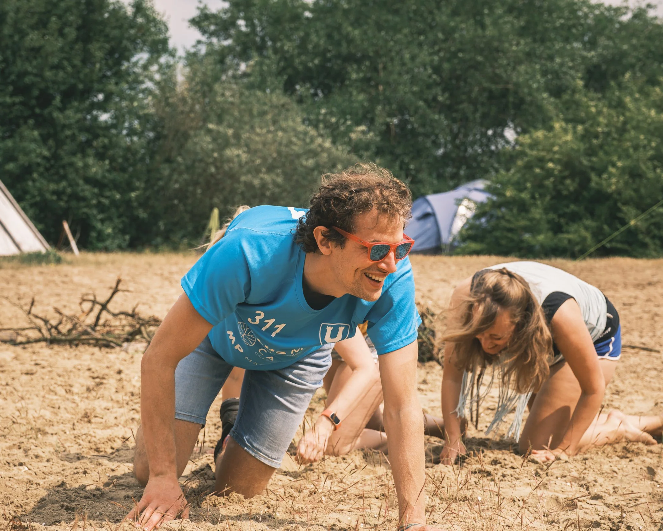 Mensen die op hun handen en knieën op zand imiteren tijdens buitenactiviteiten in een bosrijke omgeving.