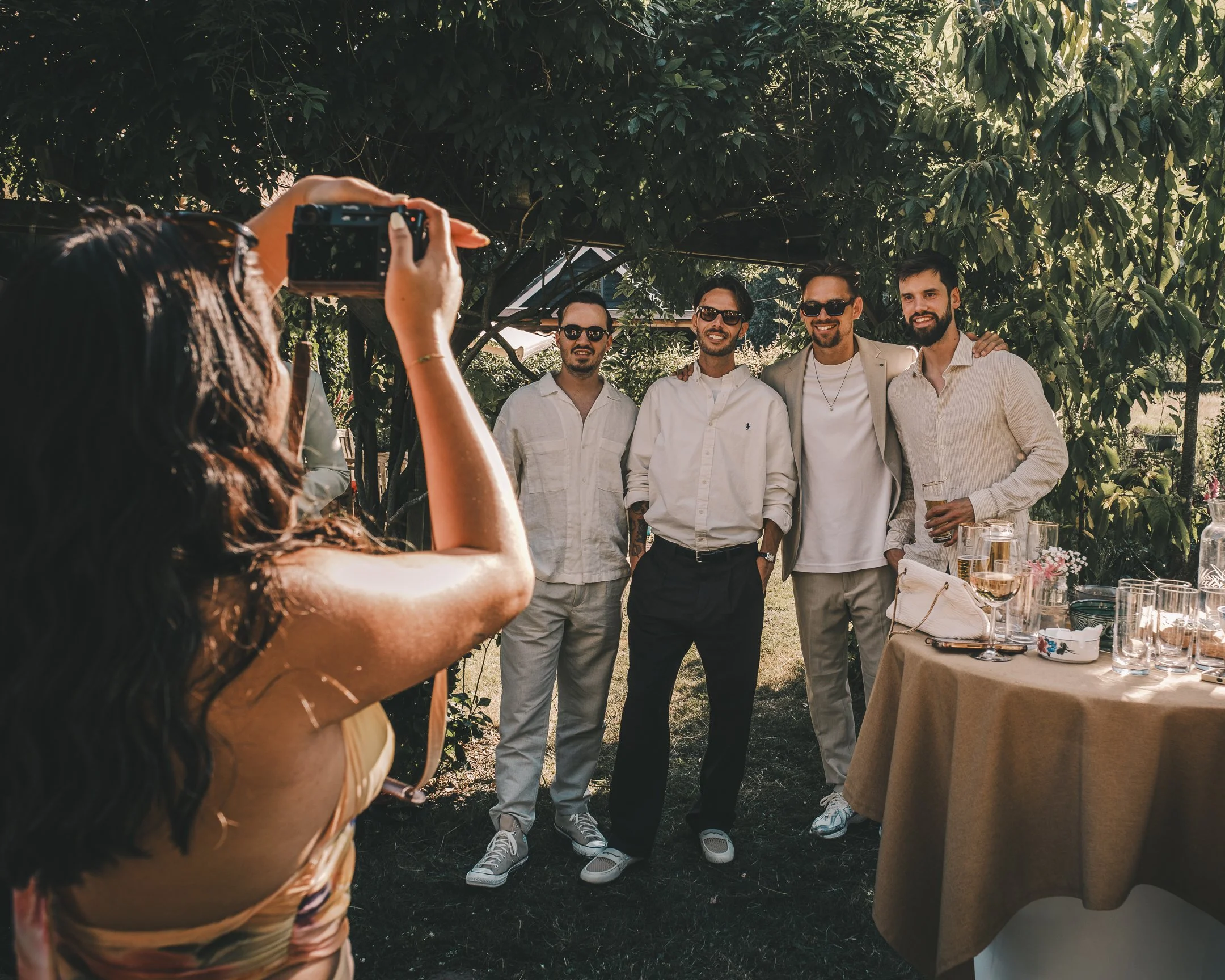 Vrouw neemt foto van een groep mannen die samen poseert buiten onder een boom tijdens een feest of bijeenkomst