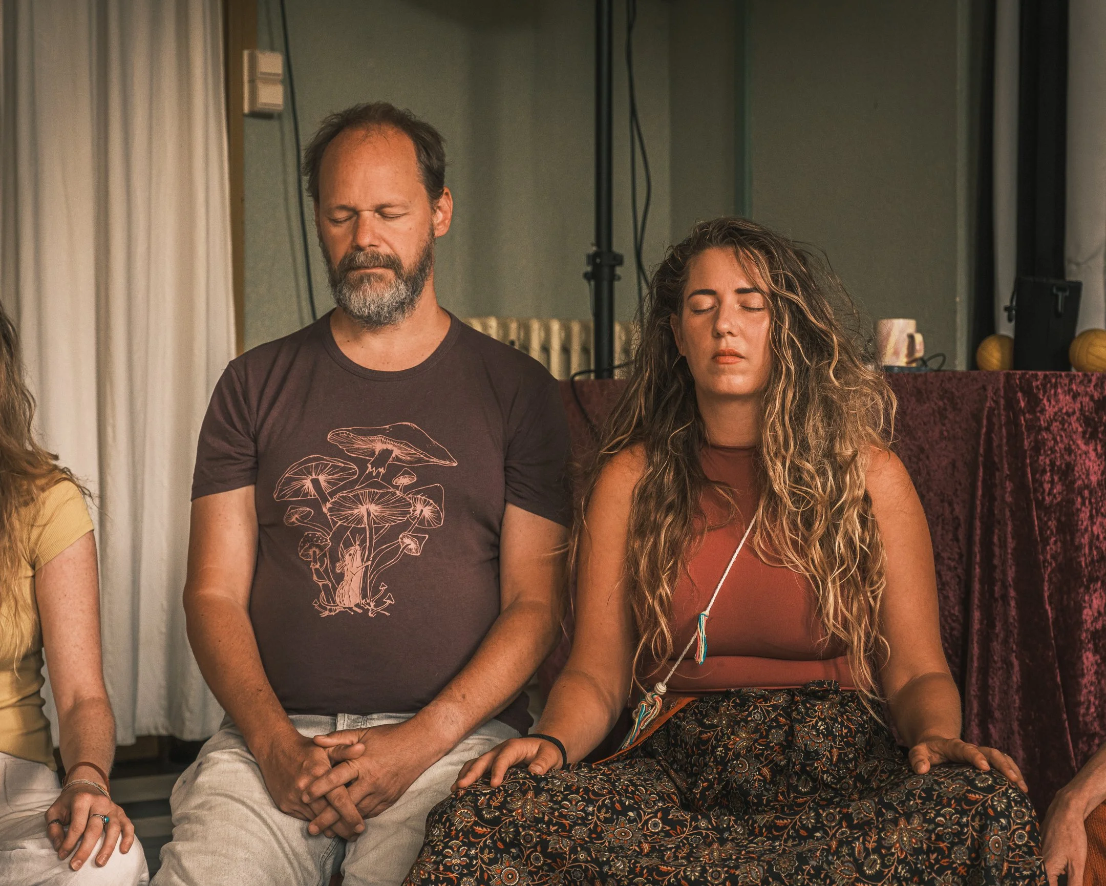 Twee mensen mediteren met gesloten ogen in een binnenruimte.