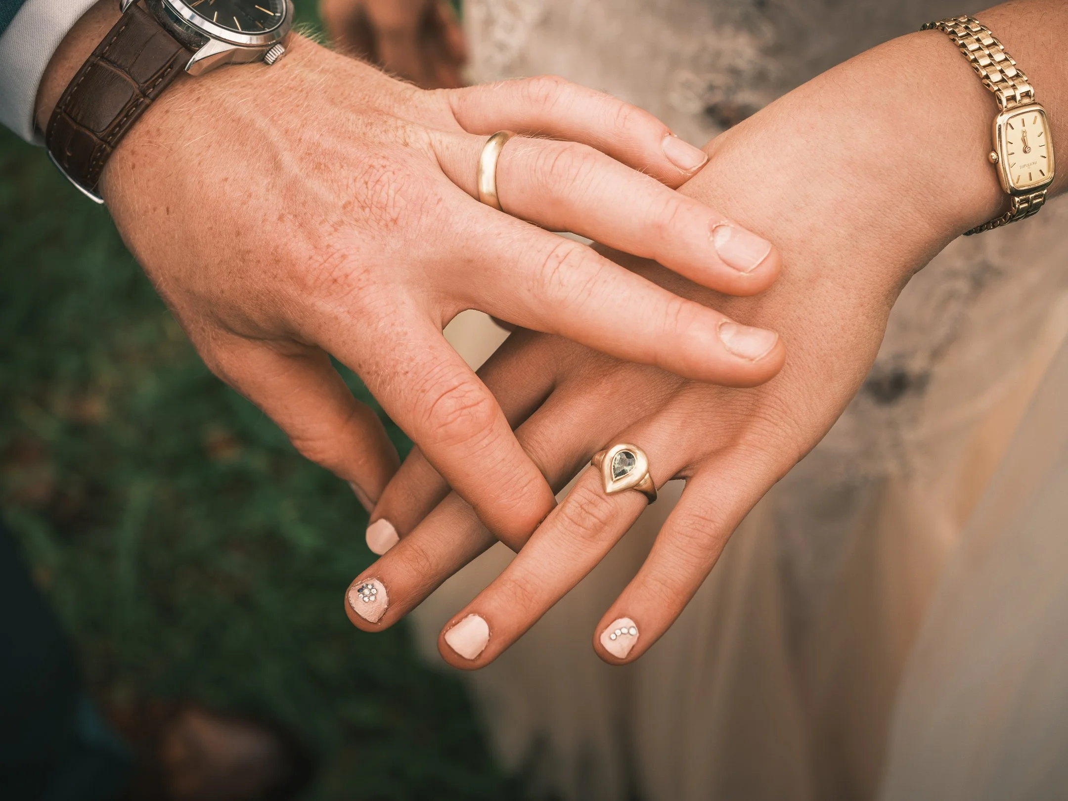 Twee mensen houden elkaars handen vast, met op de achtergrond een groene en stenen omgeving.