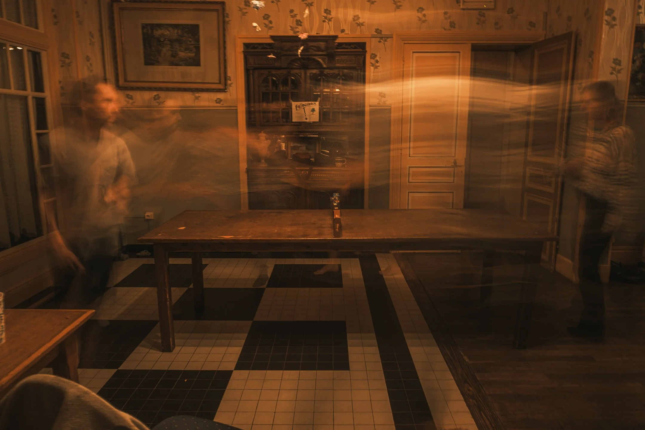 Een groep mensen die bewegen en zich verplaatsen in een kamer met vintage inrichting, met een donkere en wazige sfeer.