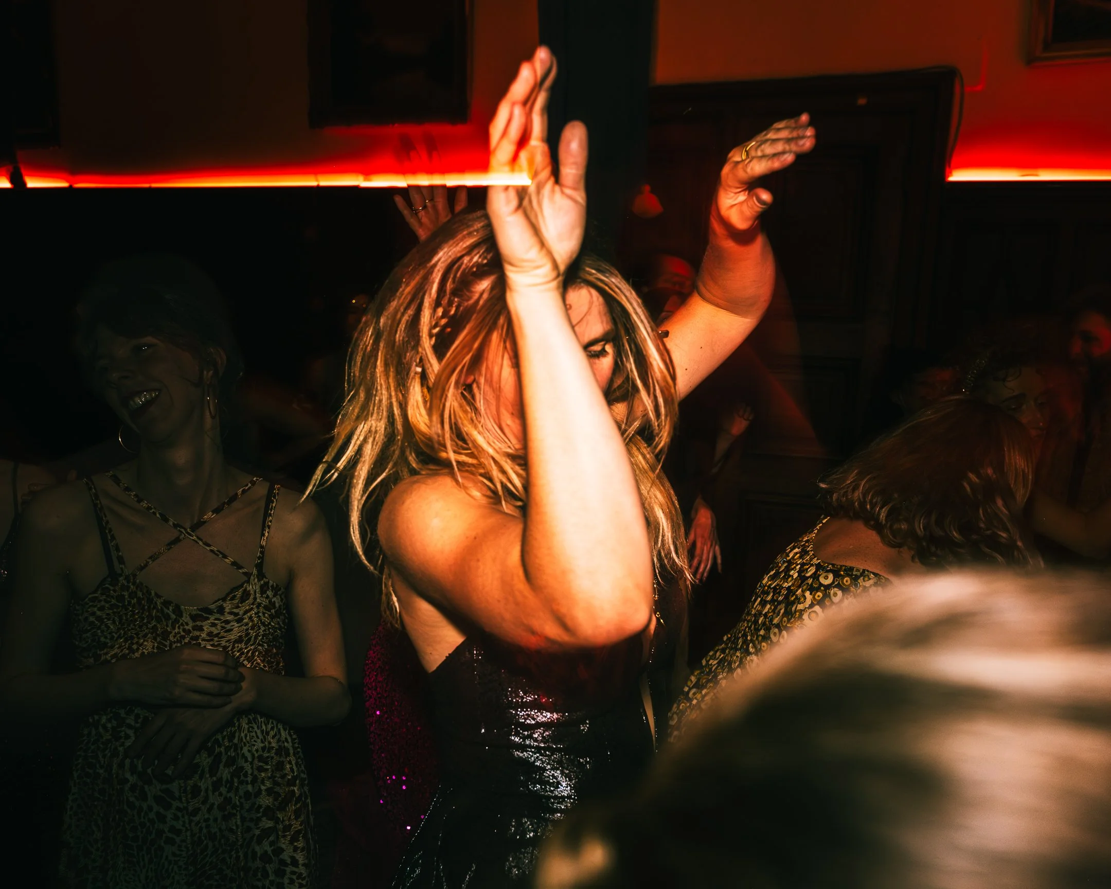 Vrouw danst in een donkere omgeving met rode verlichting, omringd door anderen die ook dansen.