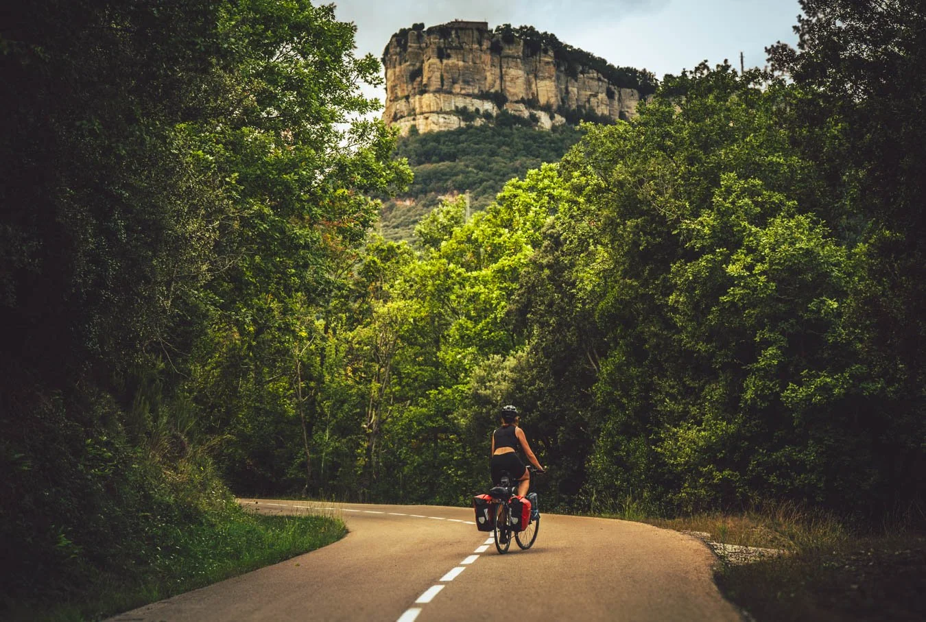 Vrouw fietst op weg door een bosrijke omgeving met een rotsformatie op de achtergrond.