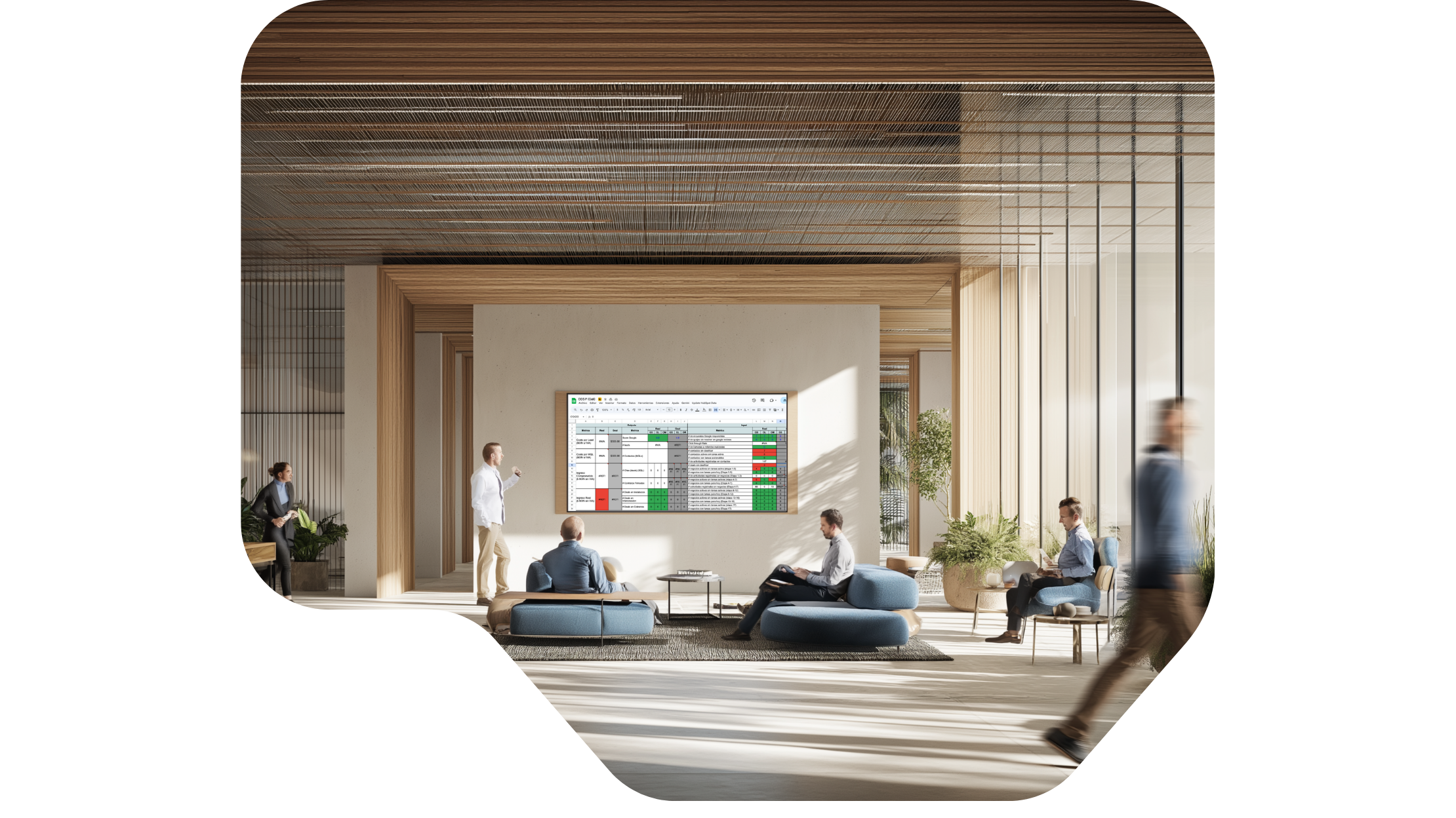Sala de reuniones moderna con varias personas conversando y trabajando, pantalla grande con hojas de cálculo en la pared, espacio con muebles azules y plantas decorativas.