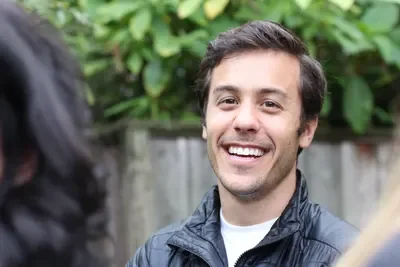 Hombre sonriendo en un ambiente exterior con vegetación.