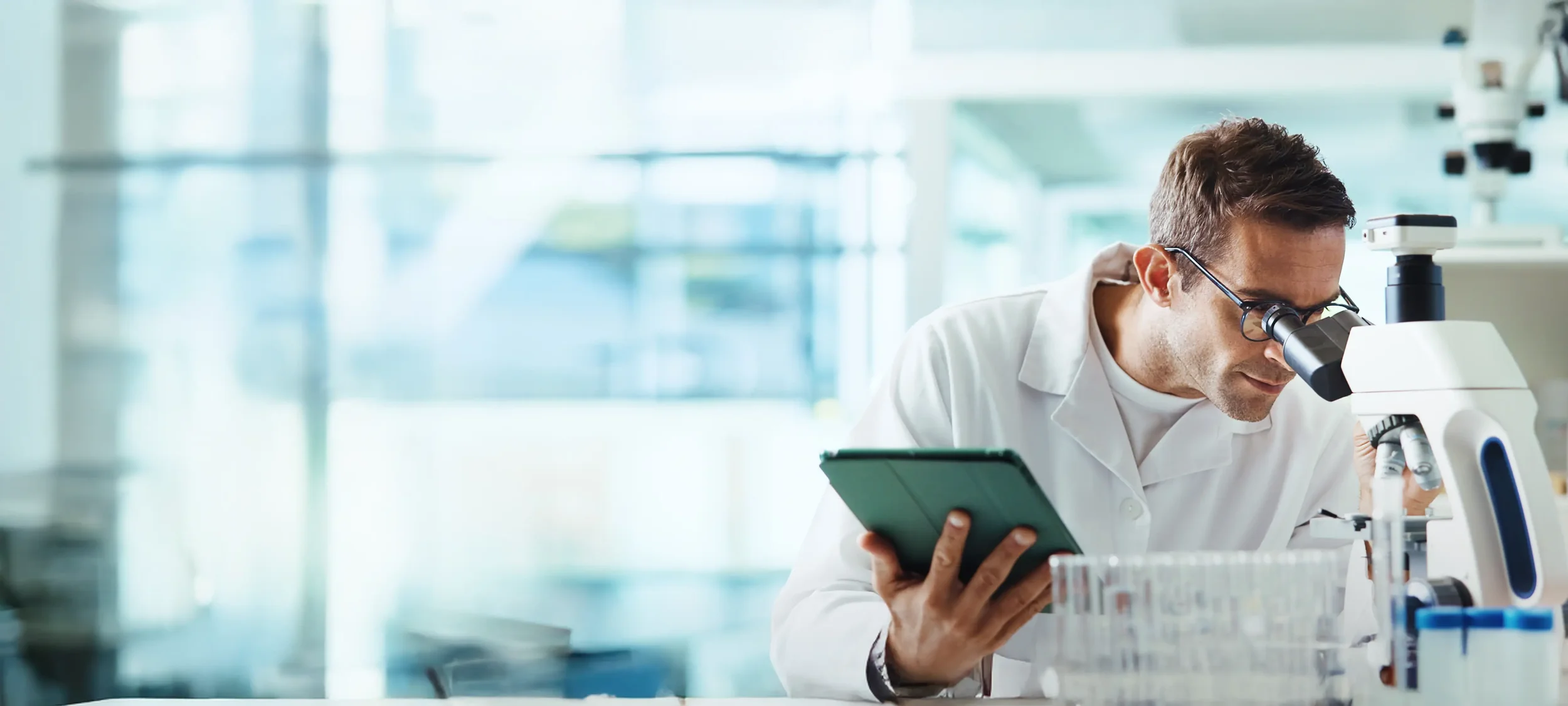 Scientist in a laboratory using a microscope and holding a tablet
