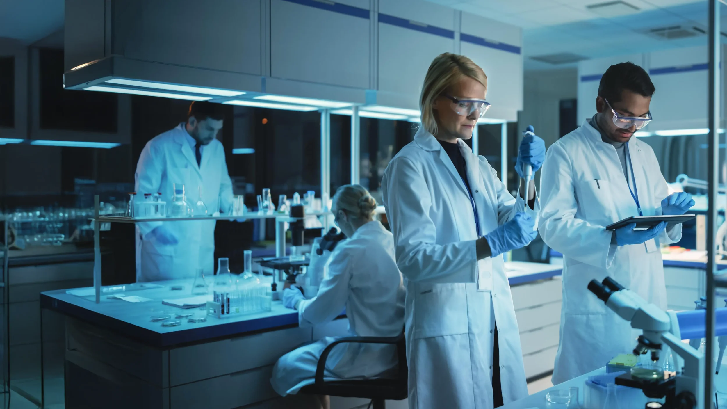 Scientists working in a modern laboratory, wearing white lab coats and safety goggles, conducting experiments with laboratory glassware and a microscope.