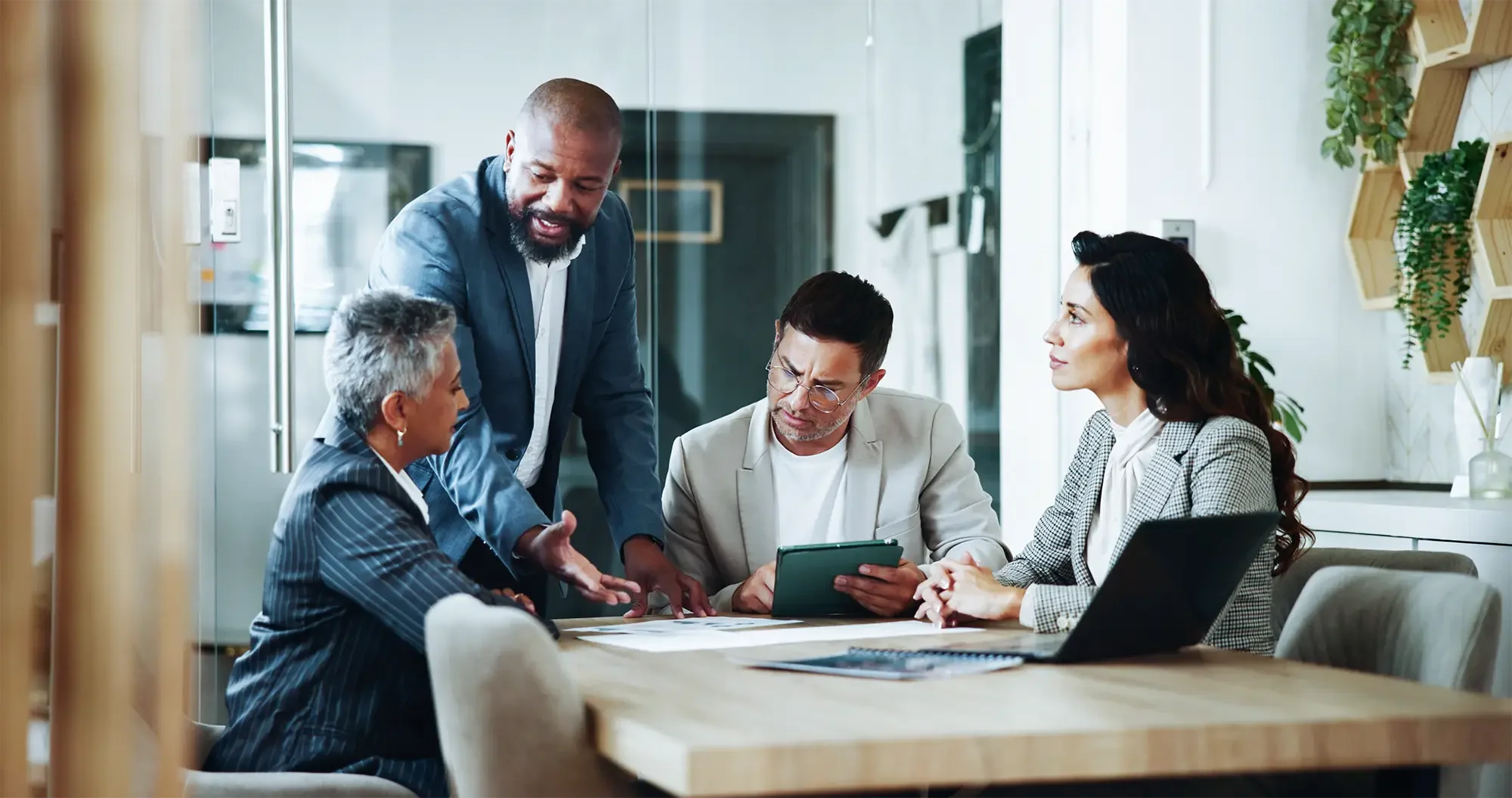Five diverse business professionals having a discussion around a table in a modern office conference room.
