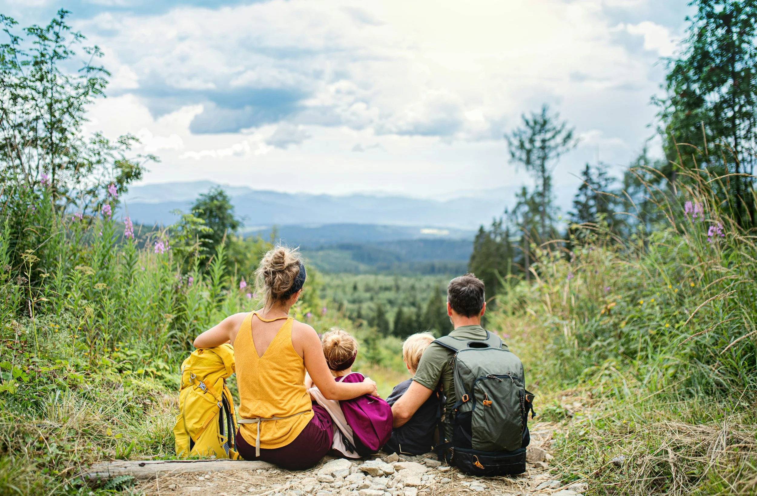 A group of hikers sitting on a trail looking at a scenic mountain view.