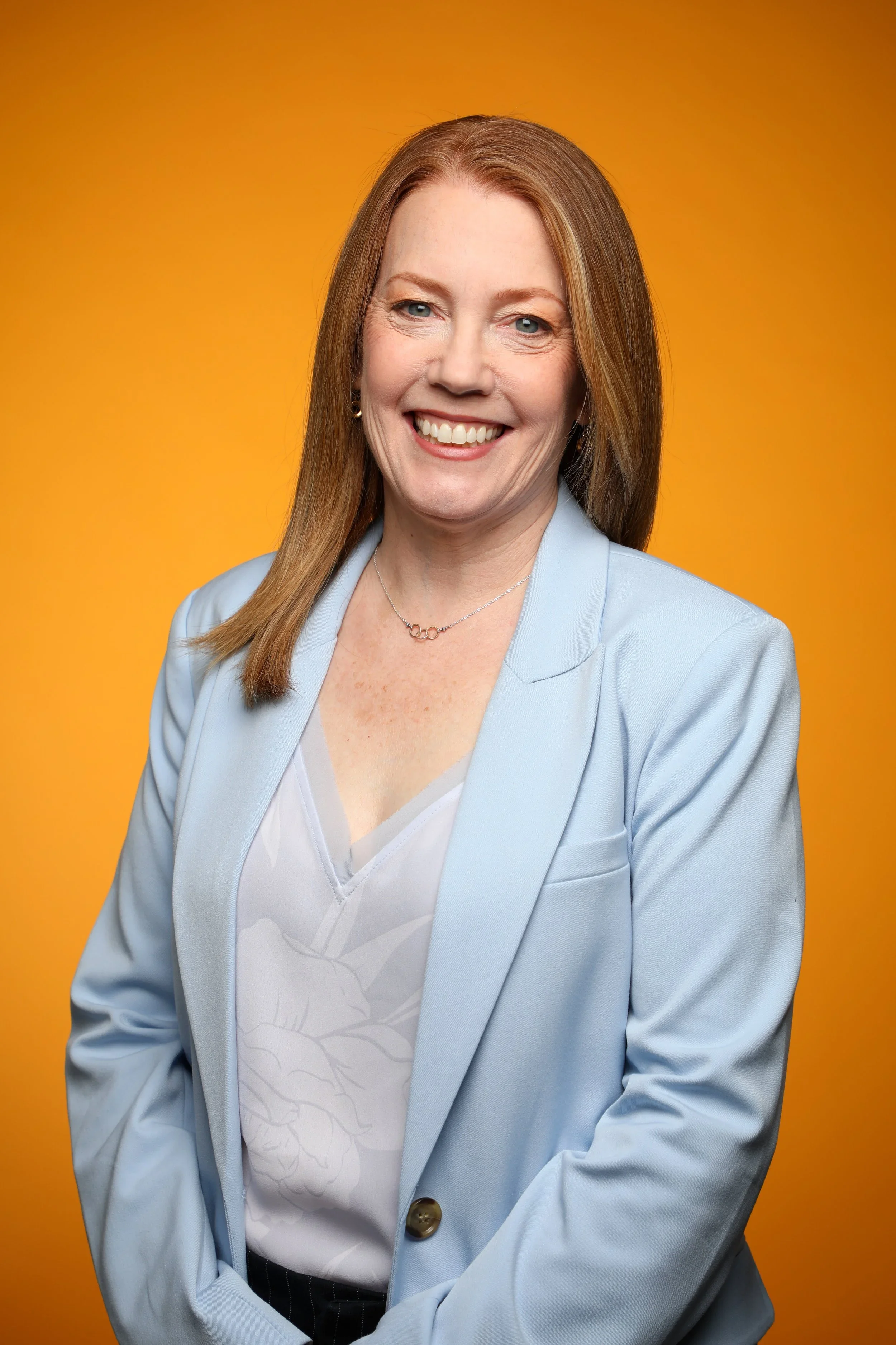 expert eos implementer beth fahey with red hair and a blue blazer smiling in front of a yellow background.