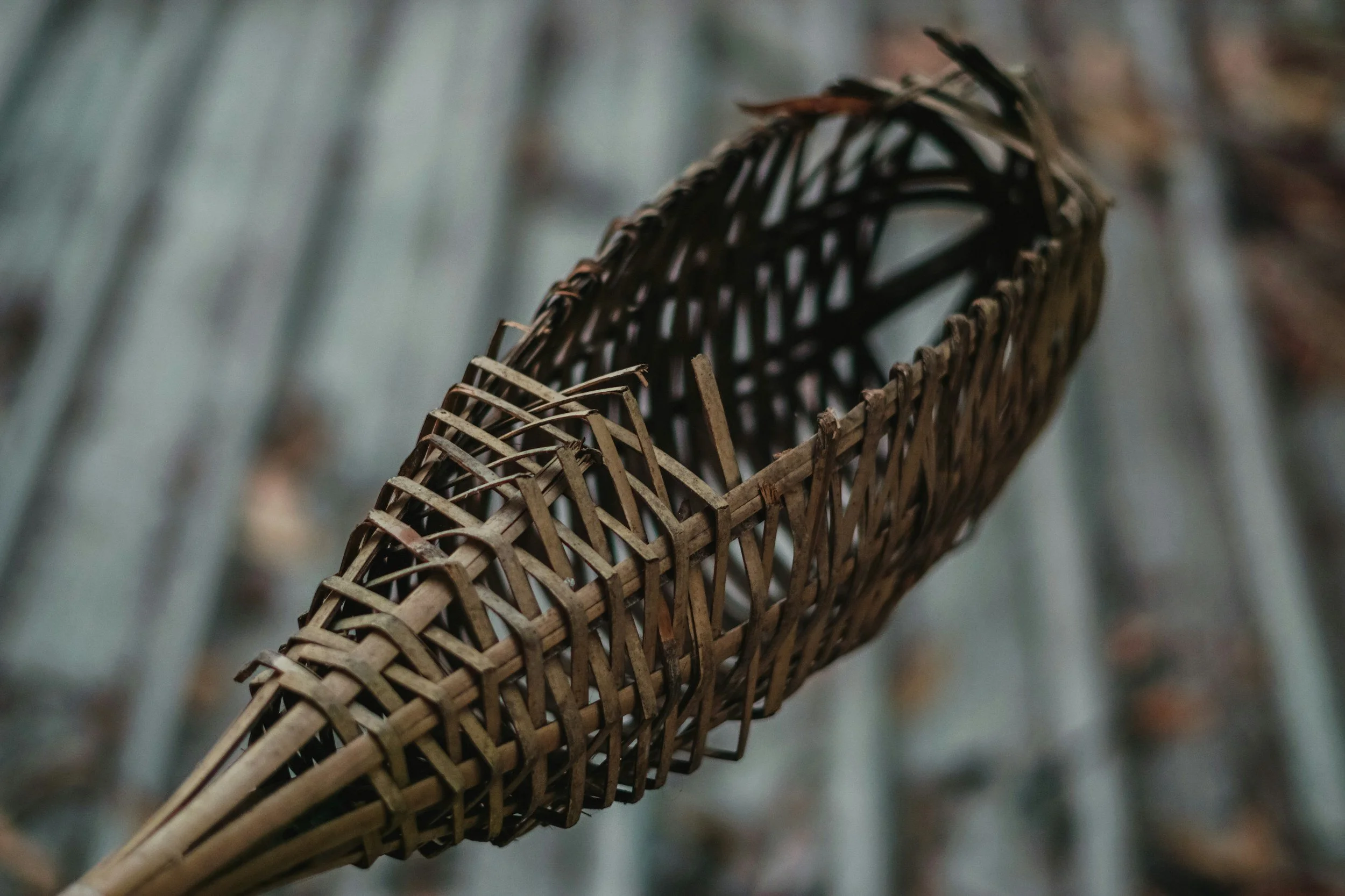 Close-up of a crafted bamboo basket or utensil with a woven design, held or resting above a blurred outdoor background.