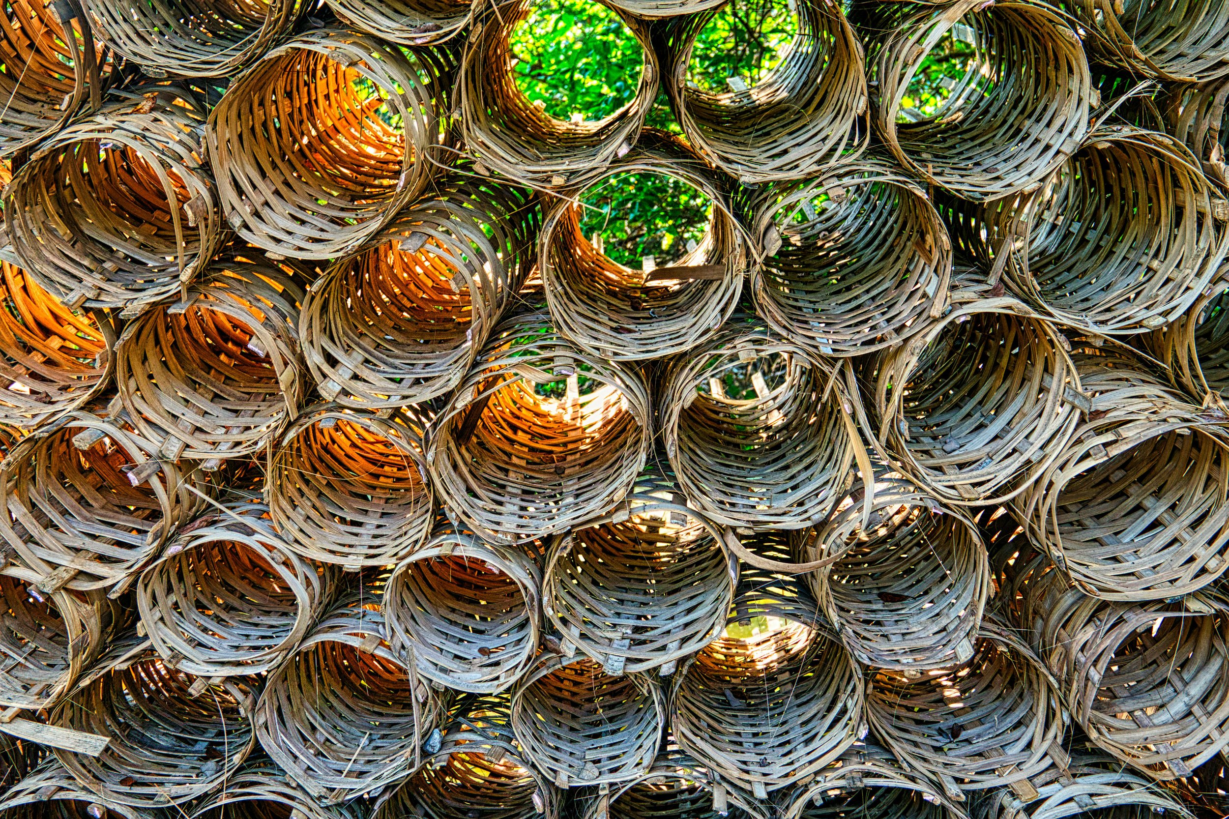 Stack of woven wicker baskets arranged outdoors with sunlight filtering through.