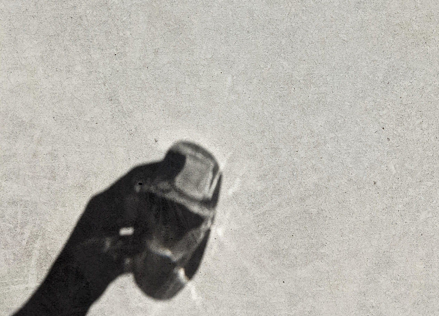 Shadow of a hand holding a small glass bottle against a textured surface.