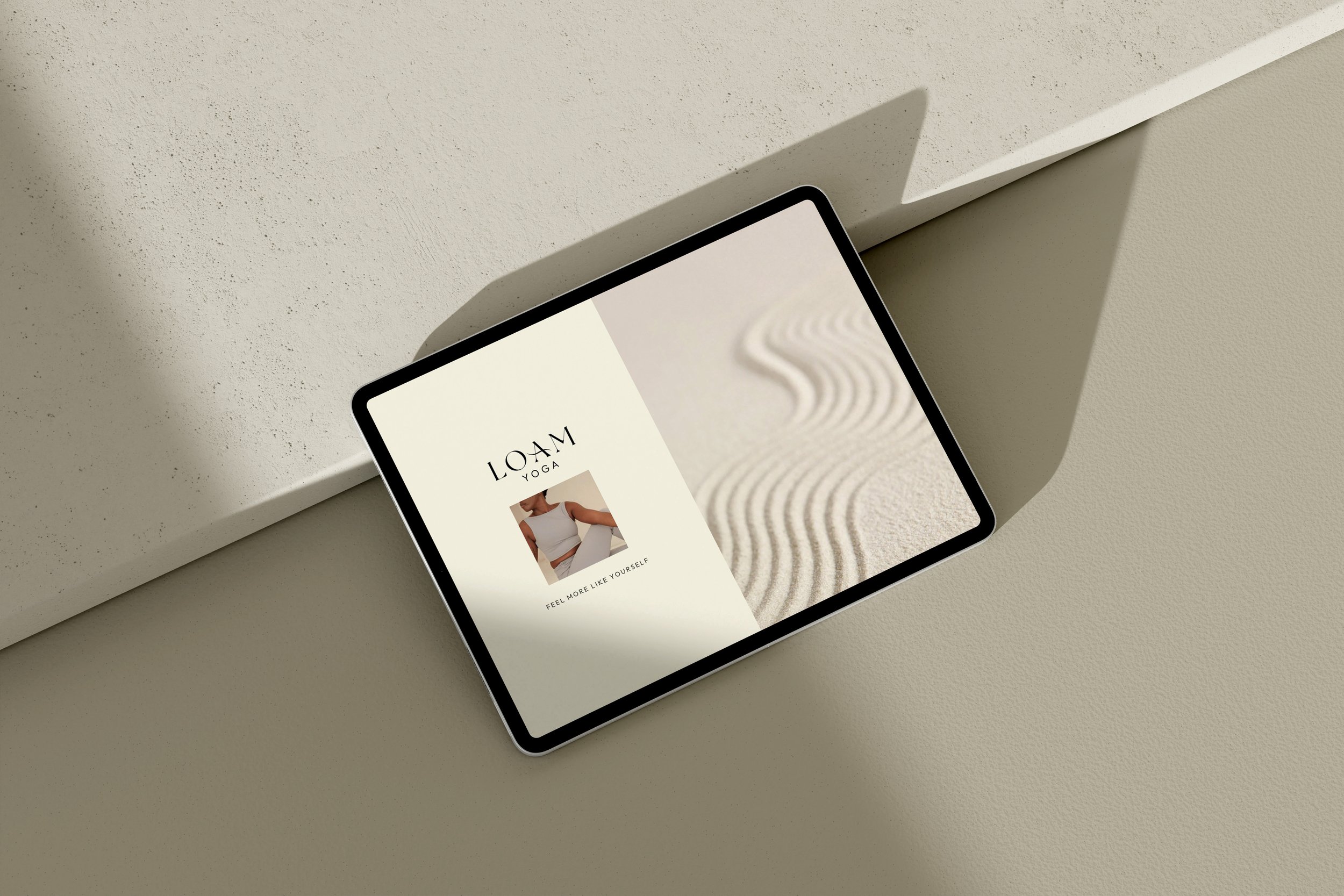 A smartphone with a yoga-themed app displayed on the screen, resting on a textured beige surface with shadow play and a background wall.